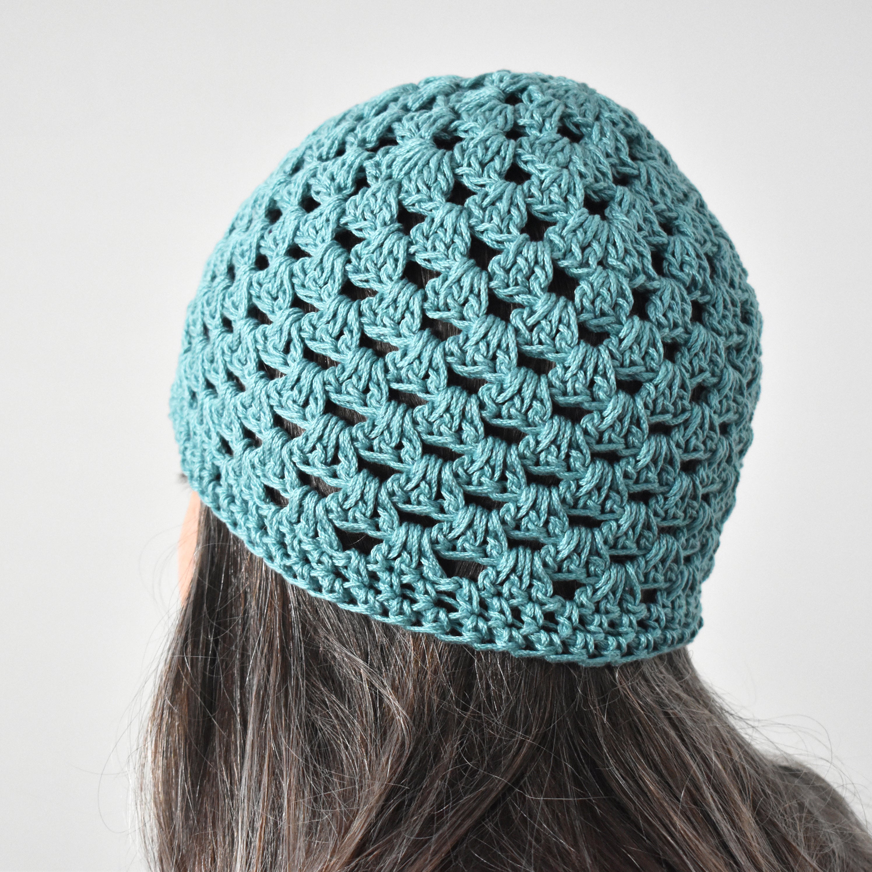Light teal crochet beanie worn by a person against a neutral background.