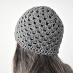 Gray knitted beanie worn by a person with long hair on a white background.