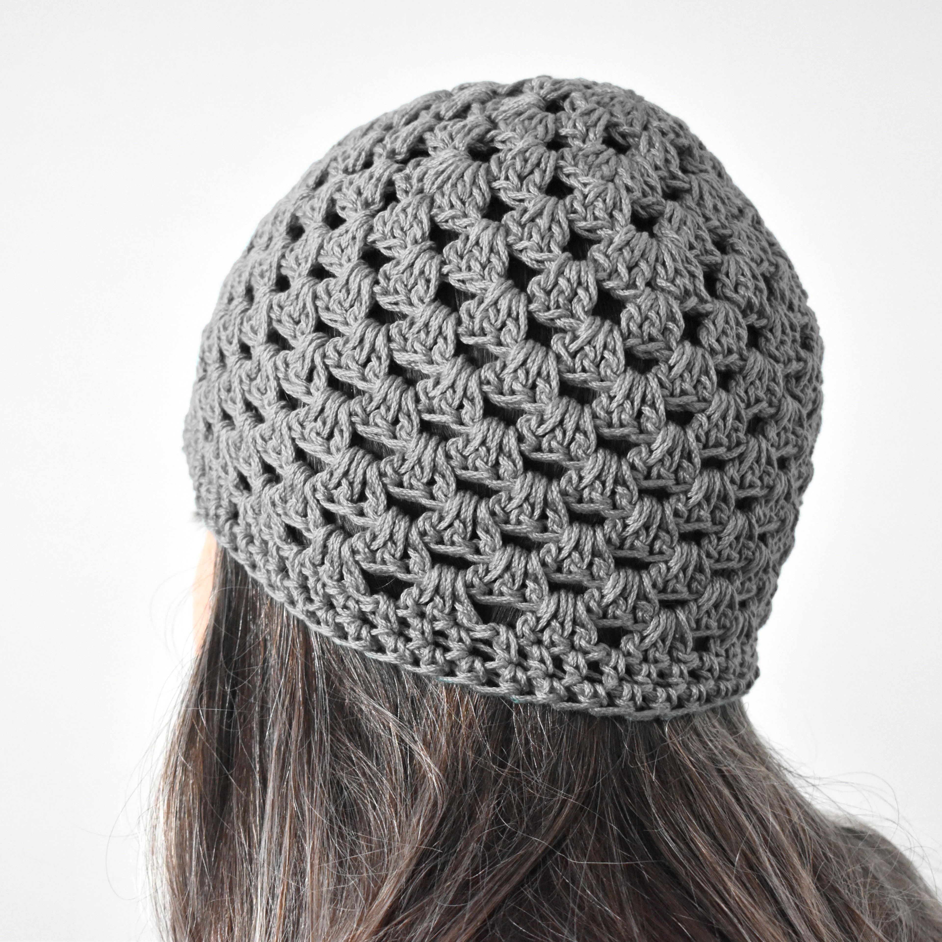 Gray knitted beanie worn by a person with long hair on a white background.