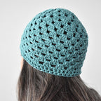 Teal crocheted beanie worn by a person with long hair against a neutral background.
