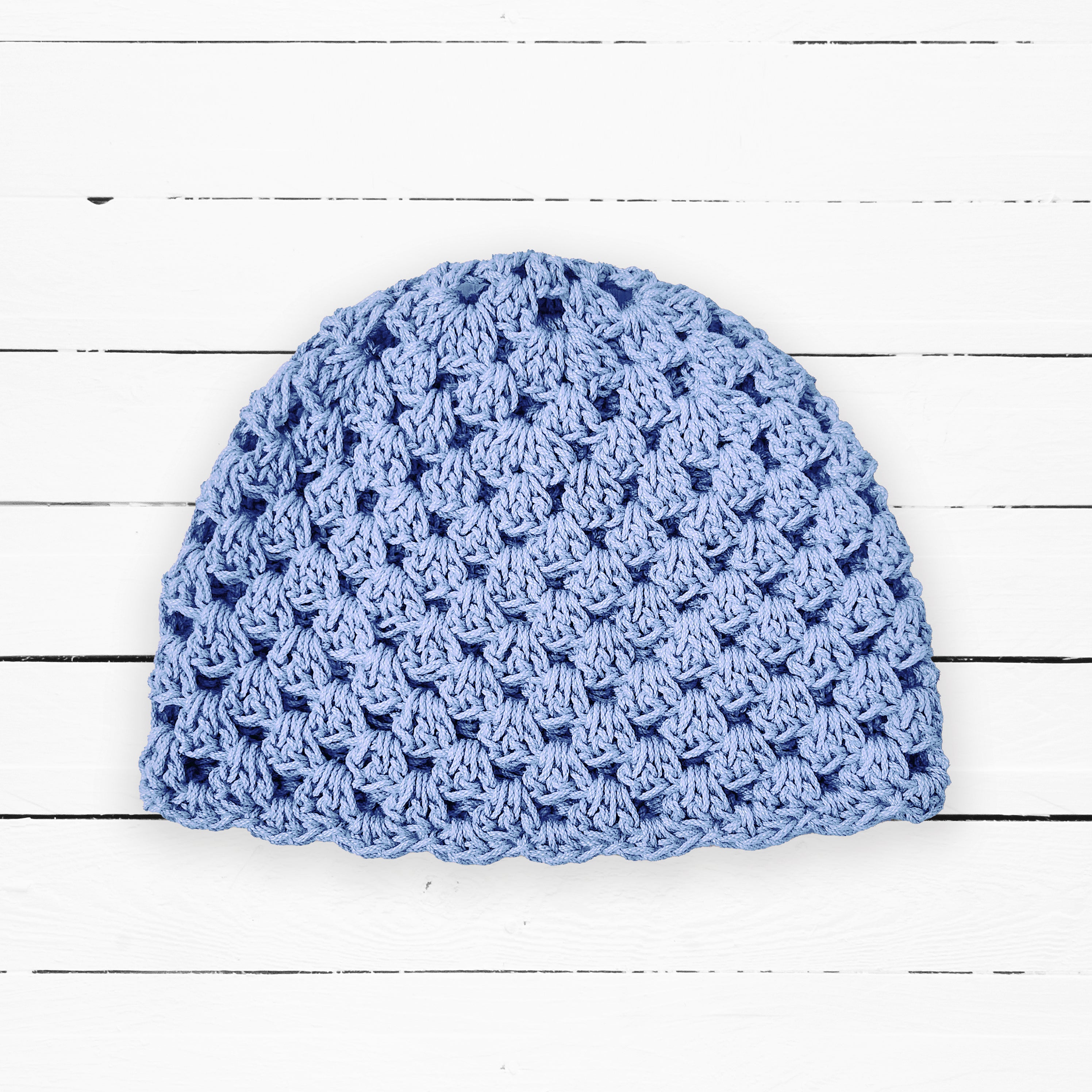 Baby blue crocheted beanie on a white wooden surface.