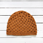 Amber orange crochet beanie on a white wooden surface.