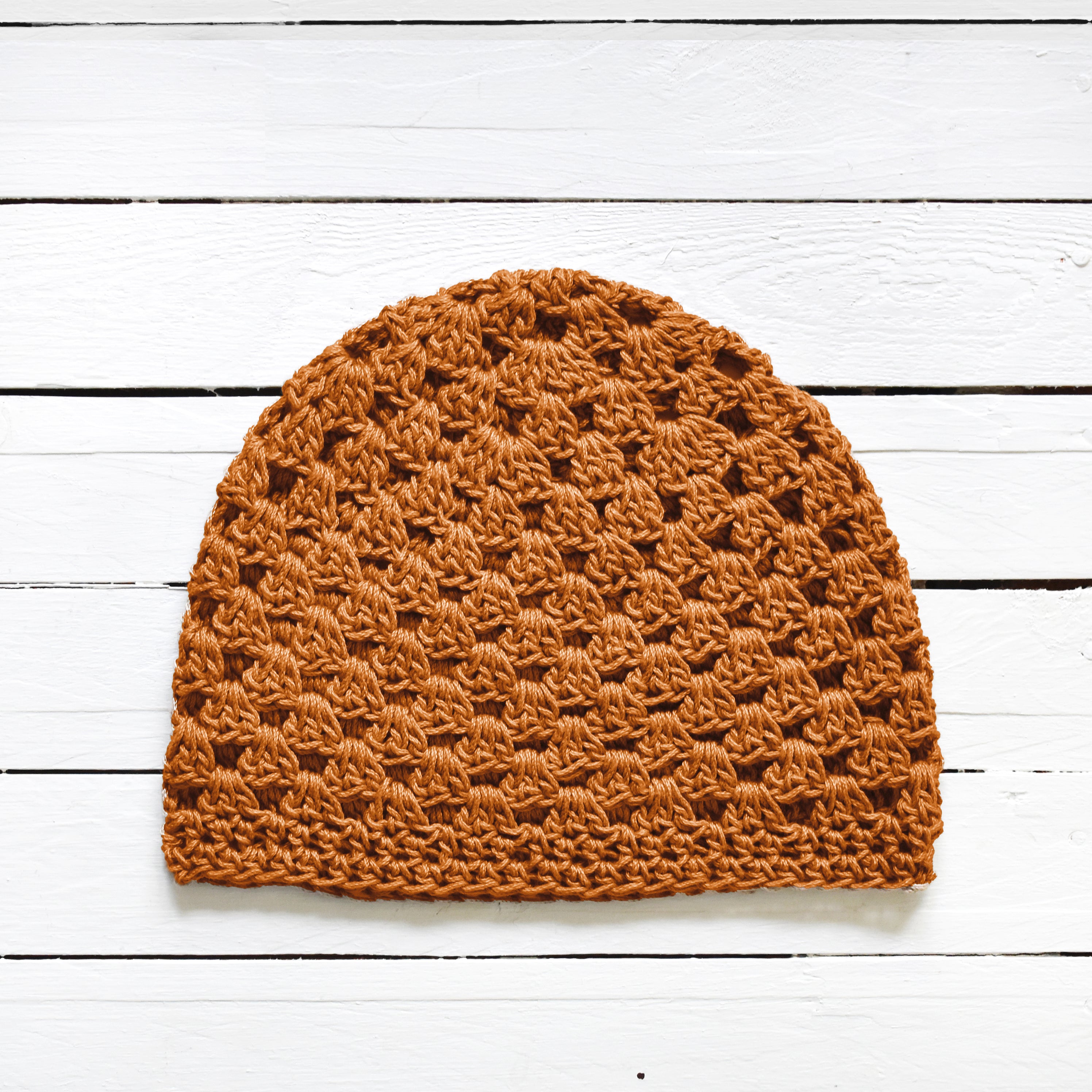Amber orange crochet beanie on a white wooden surface.