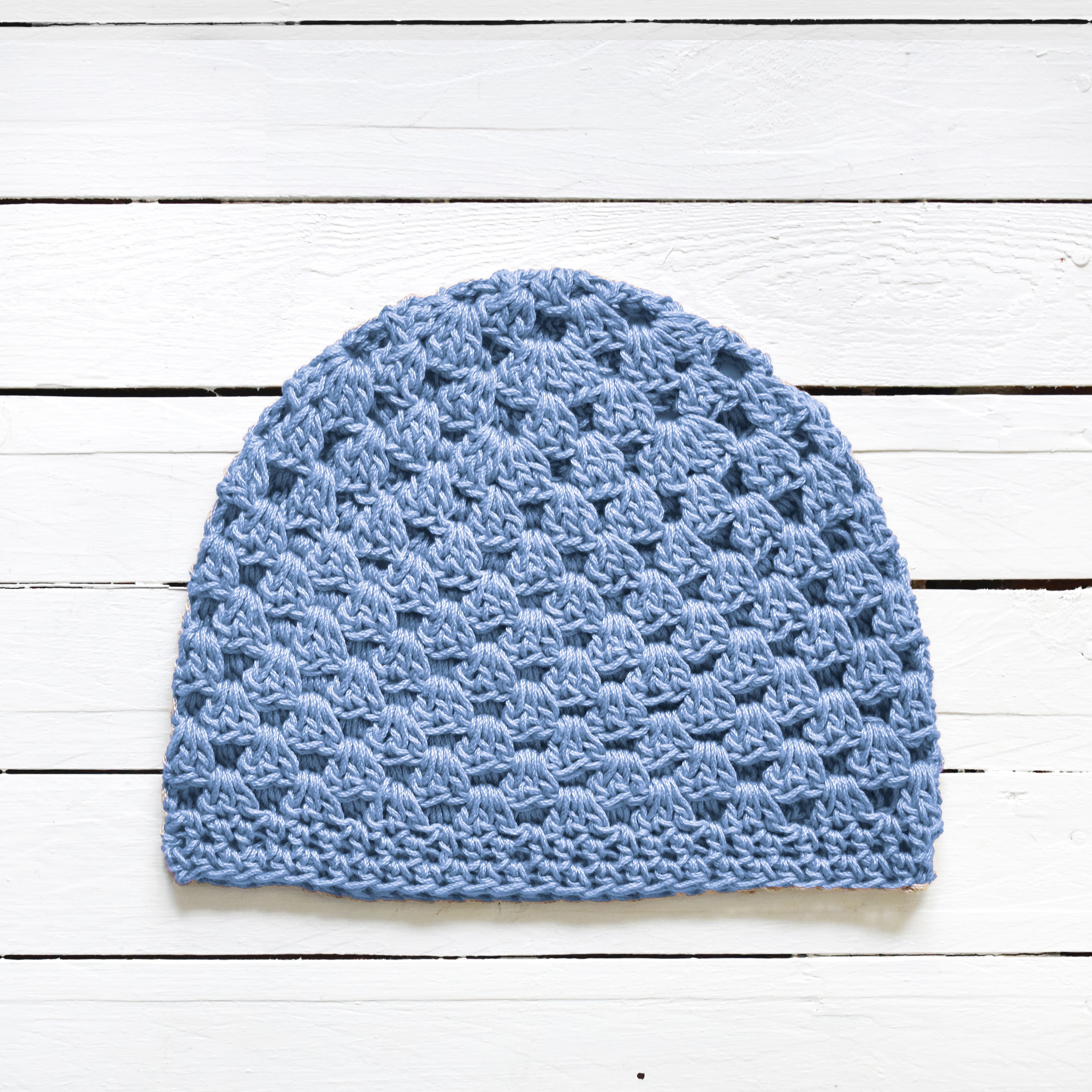 Baby blue crochet beanie on a white wooden surface.