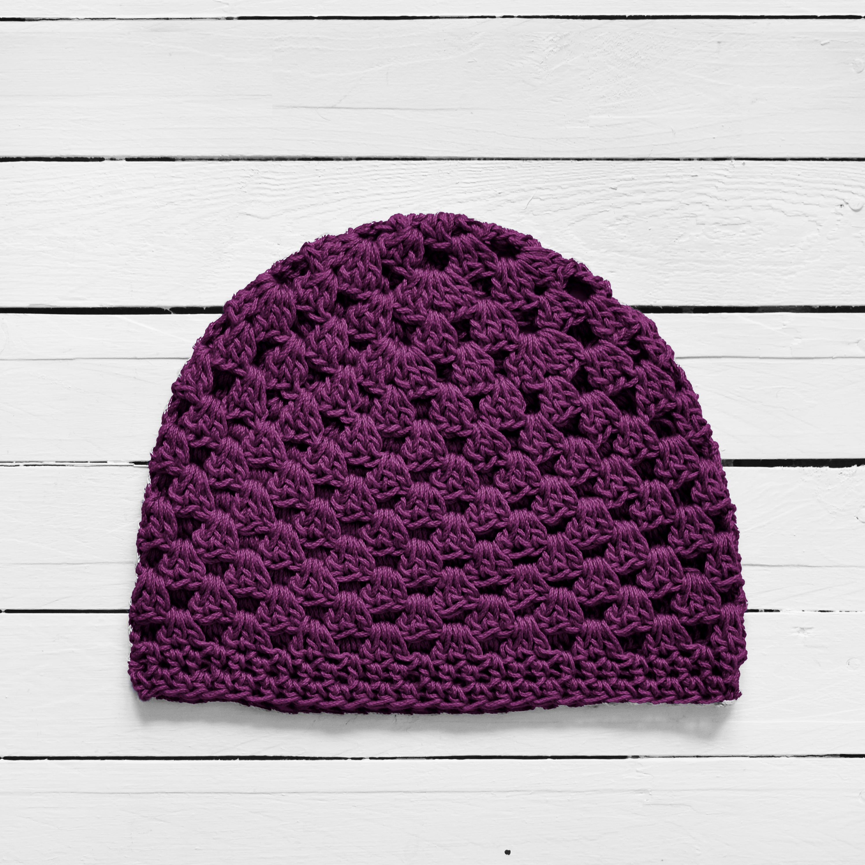 Dark purple knitted beanie on a white wooden surface.