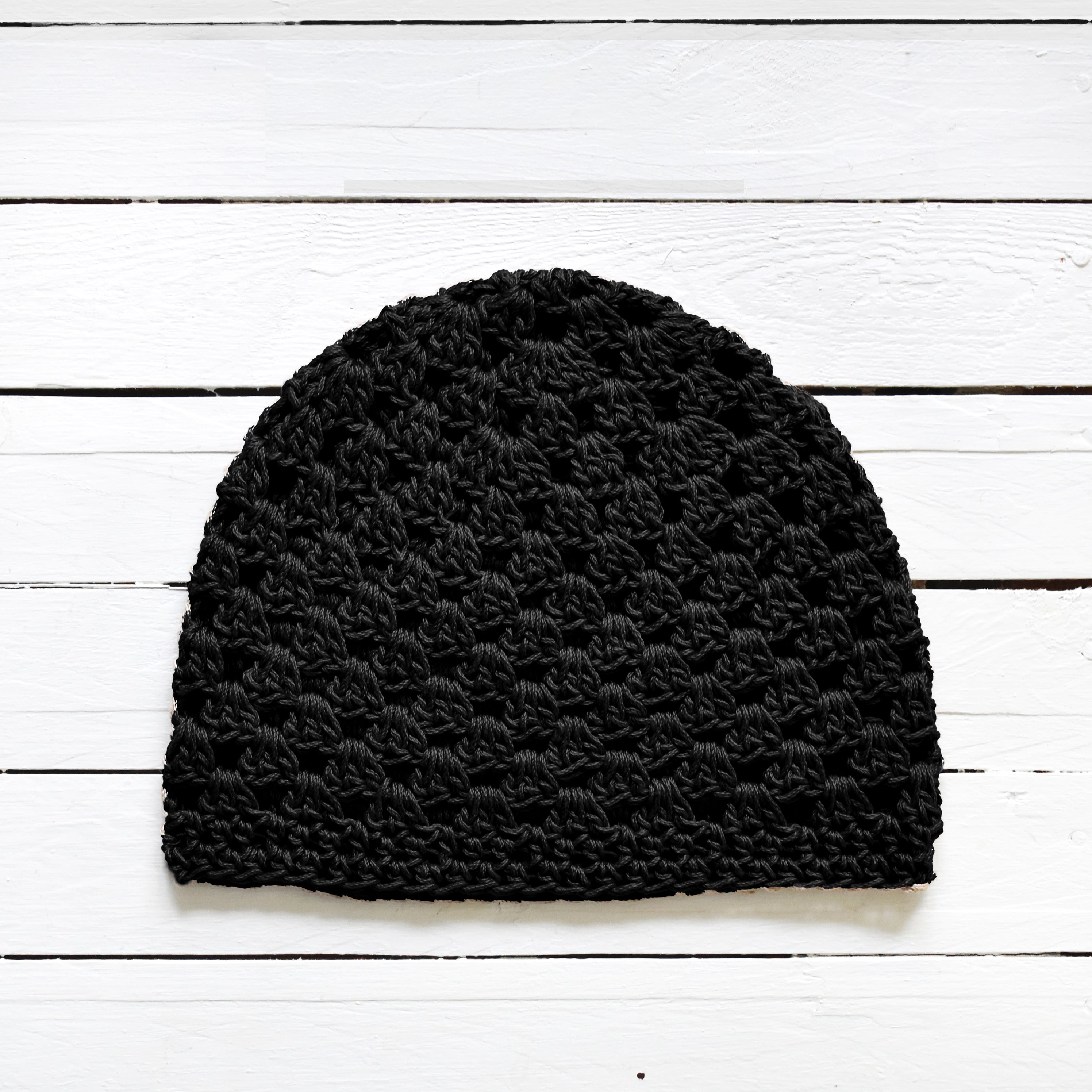 Black crochet beanie on a white wooden surface.