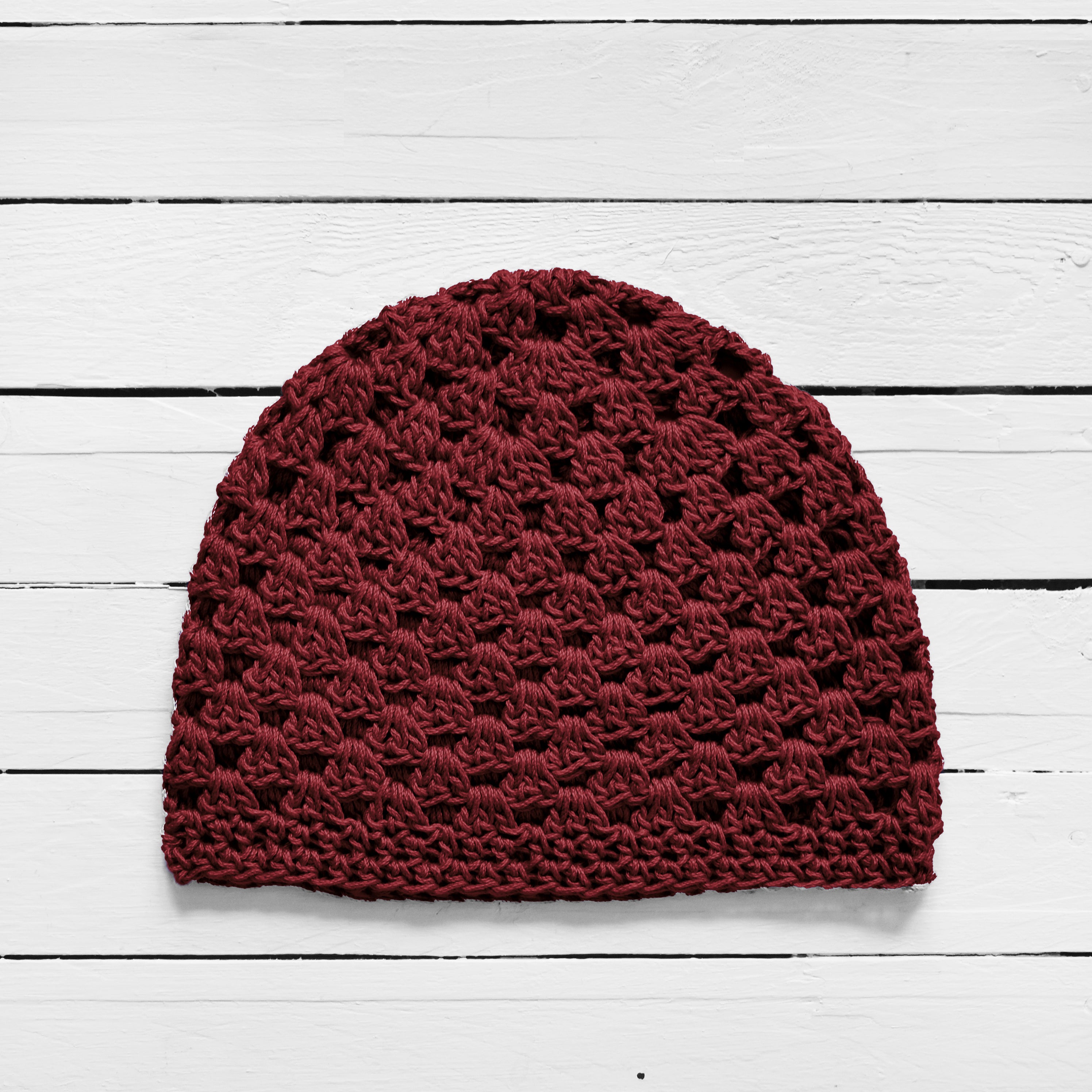 Burgundy red knitted beanie on a white wooden surface.