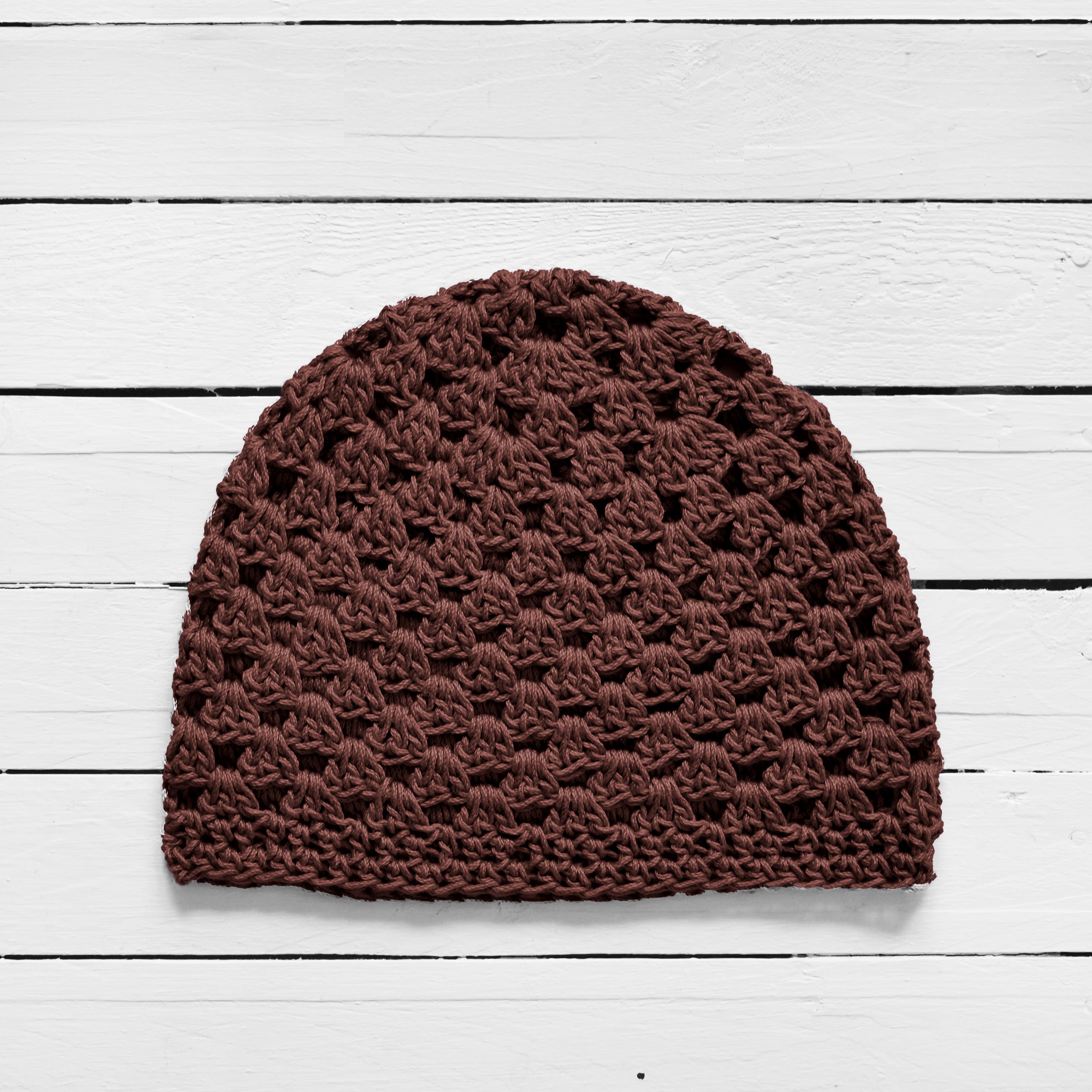 Brown knitted beanie on a white wooden surface.