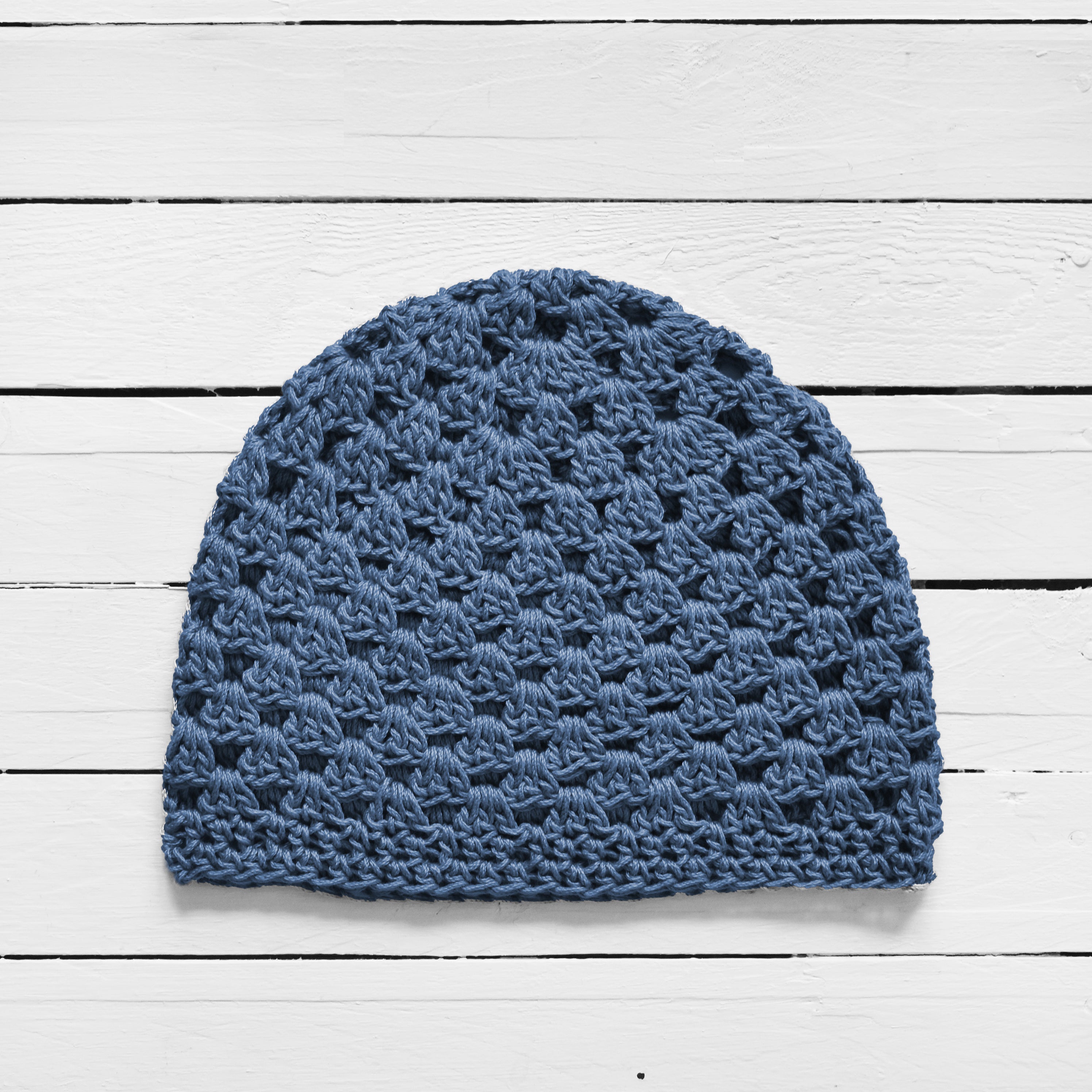 Gray-blue crocheted beanie on a white wooden surface.