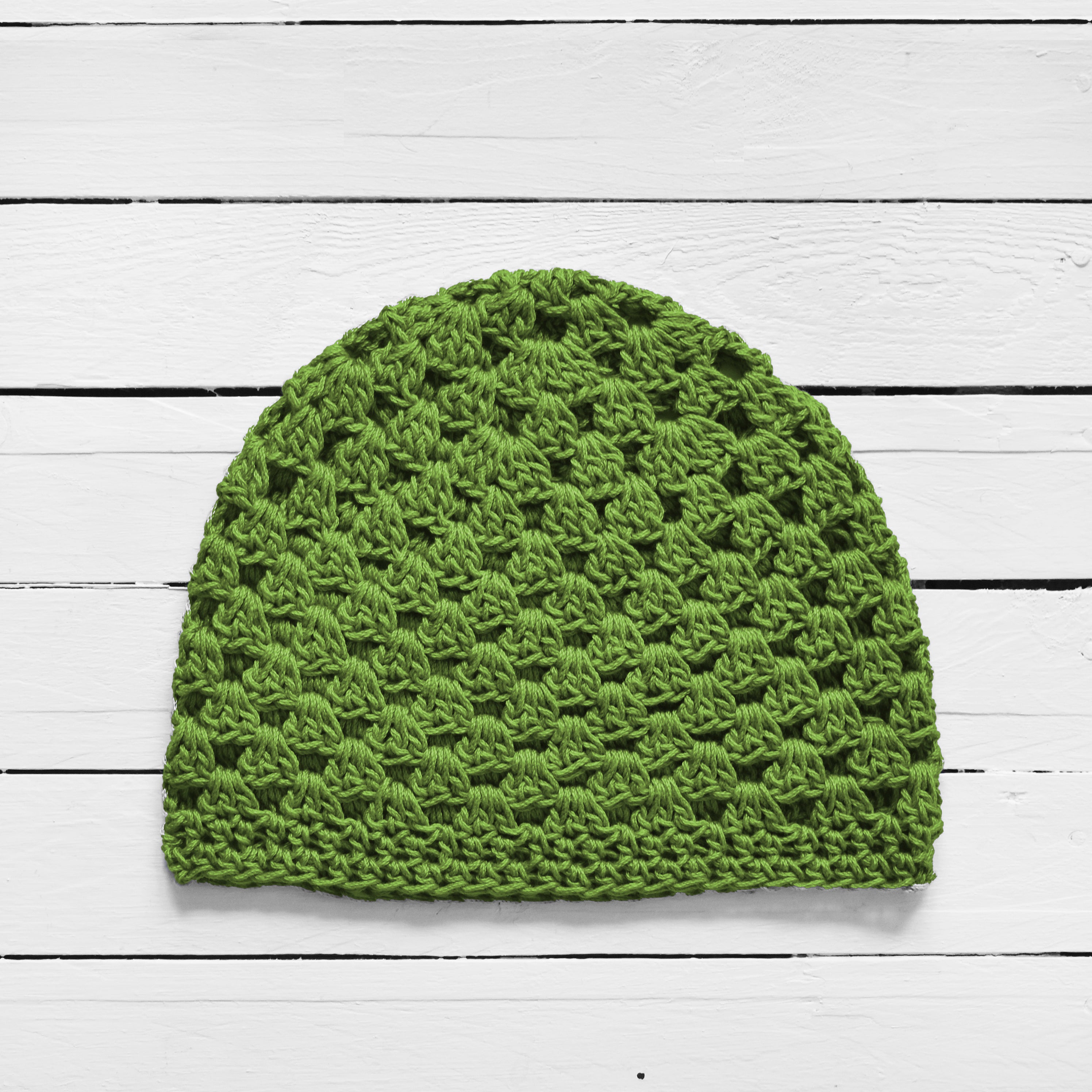 Green crochet beanie on a white wooden surface.
