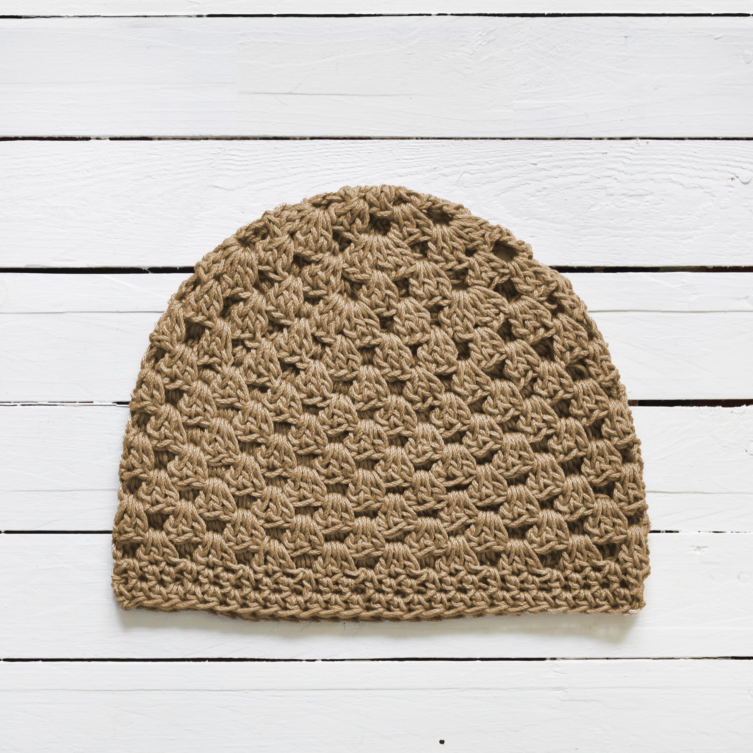 Tan crochet beanie on a white wooden surface.