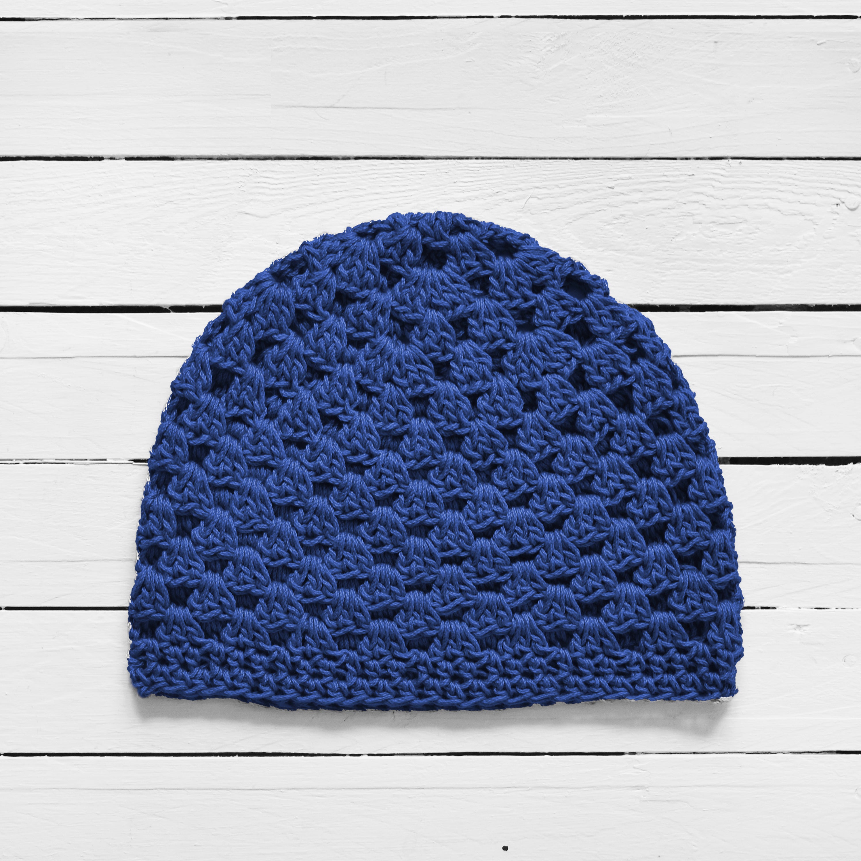 Blue crocheted beanie on a white wooden surface.