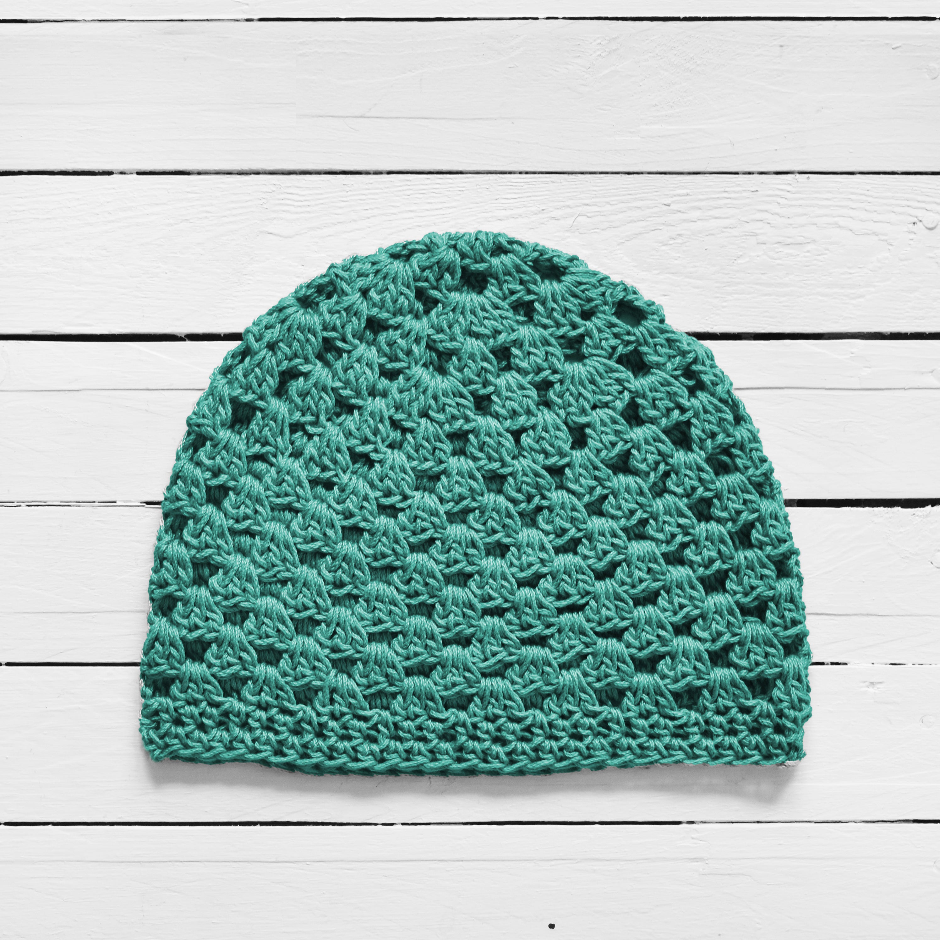Light teal crochet beanie on a white wooden surface.