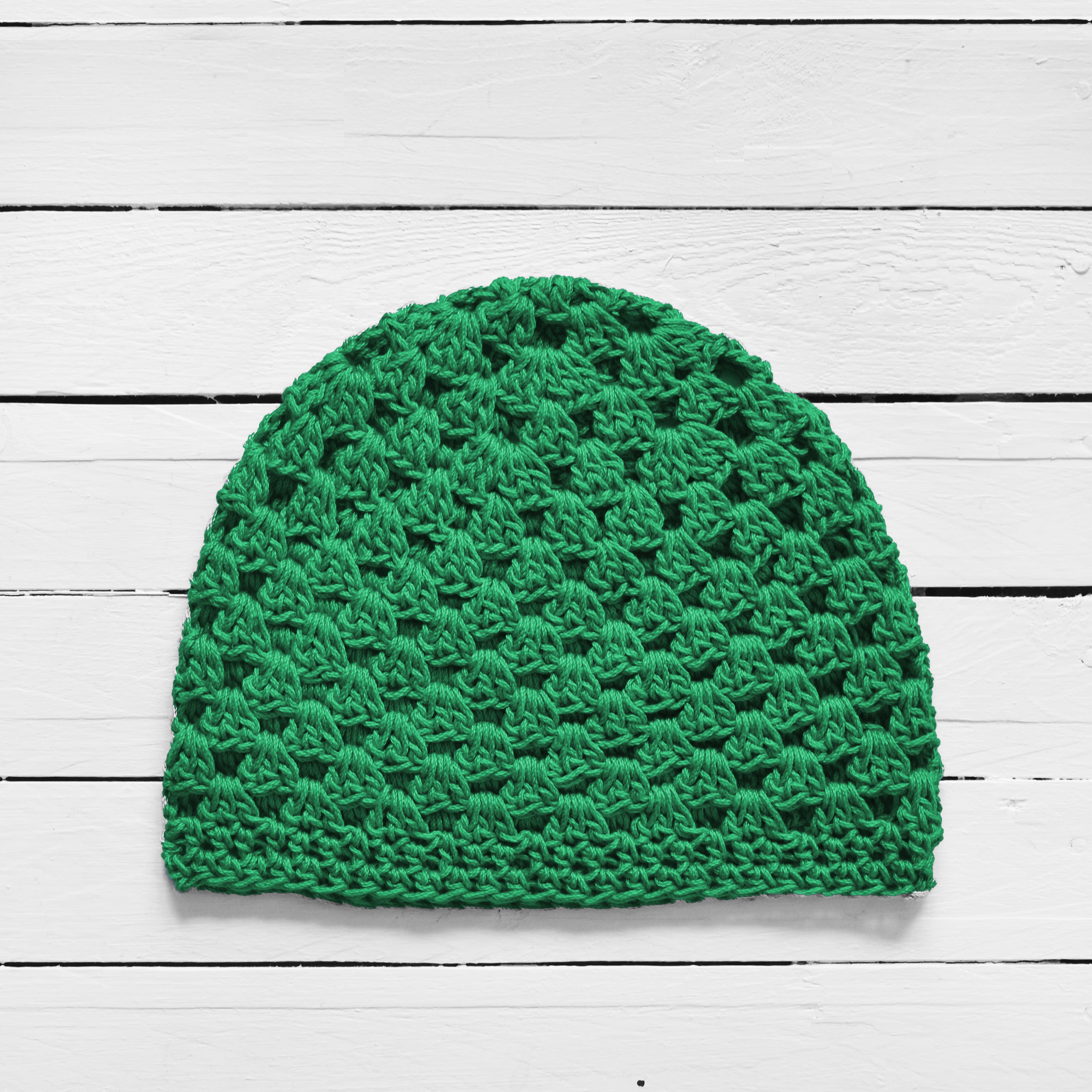 Green knitted beanie on a white wooden surface.
