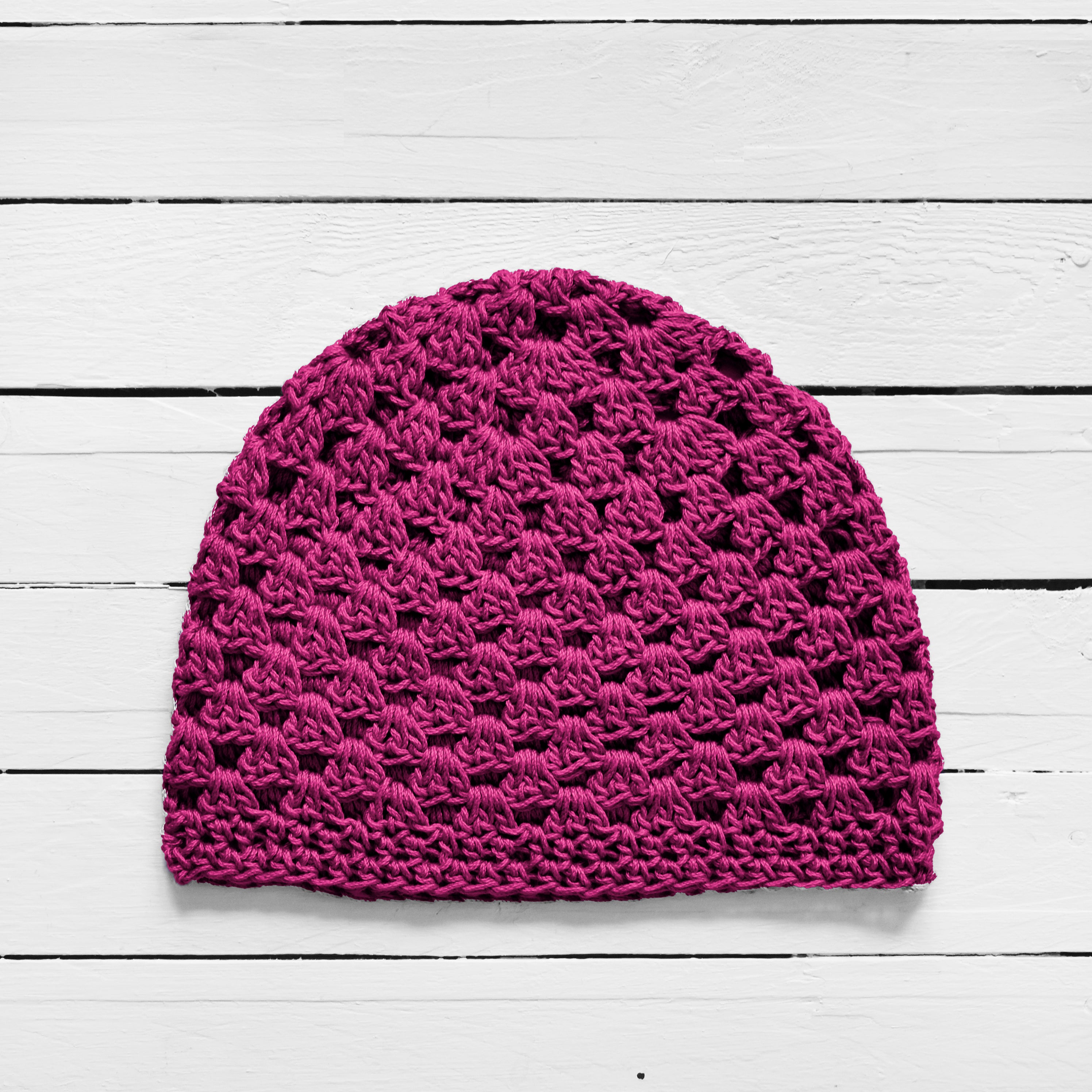 Magenta pink crochet beanie on a white wooden surface.
