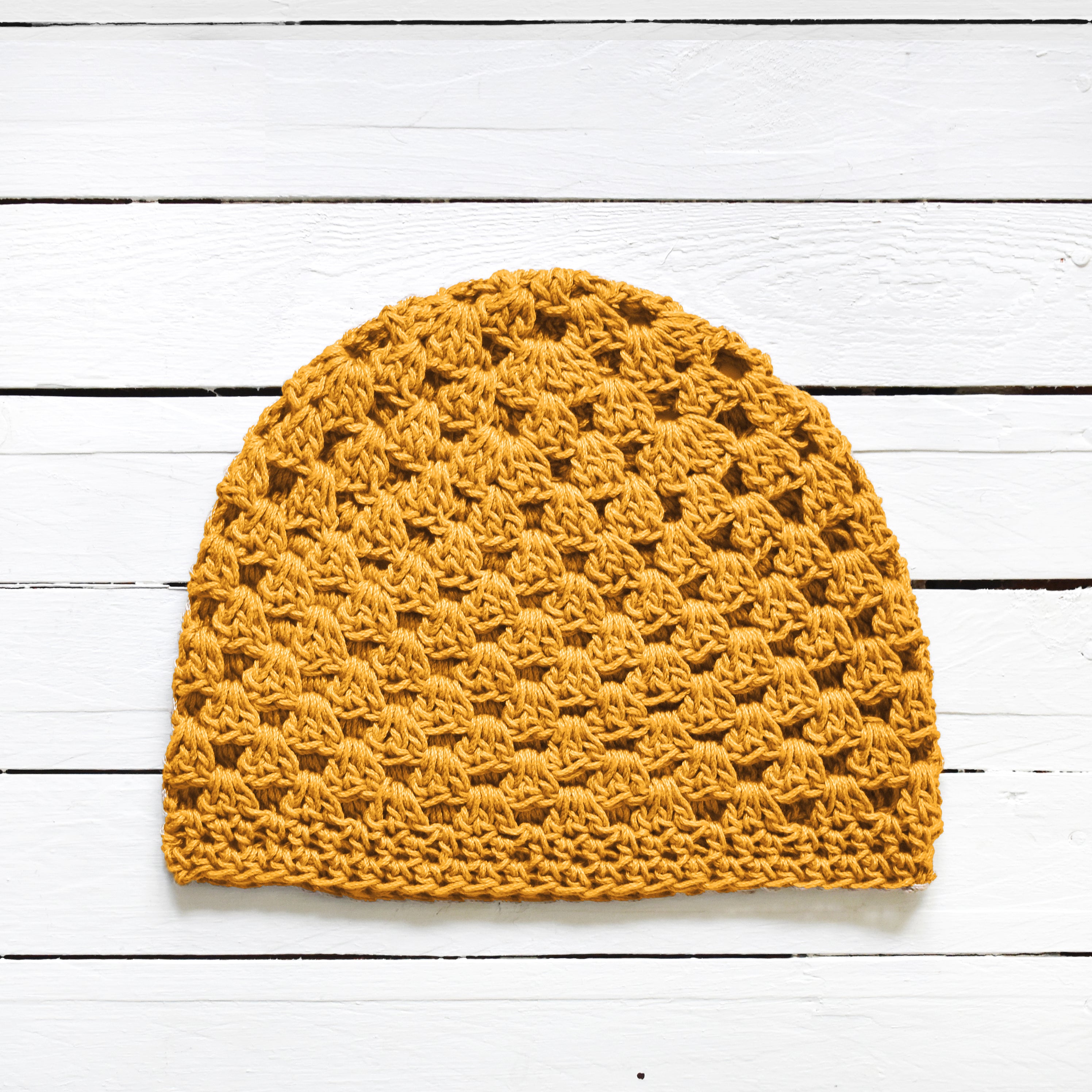 Yellow crochet beanie on a white wooden surface.