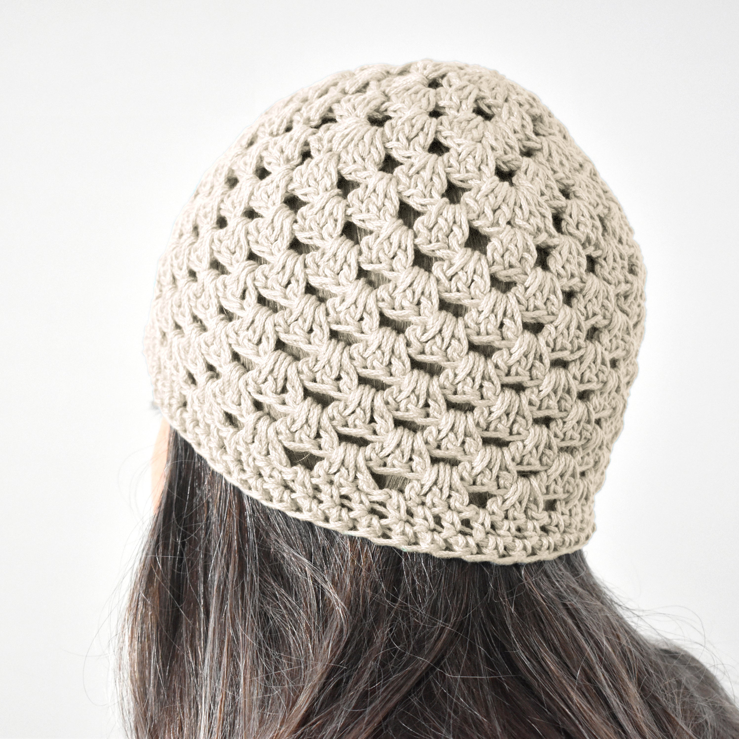 Beige crochet beanie worn by a person with long dark hair on a white background.
