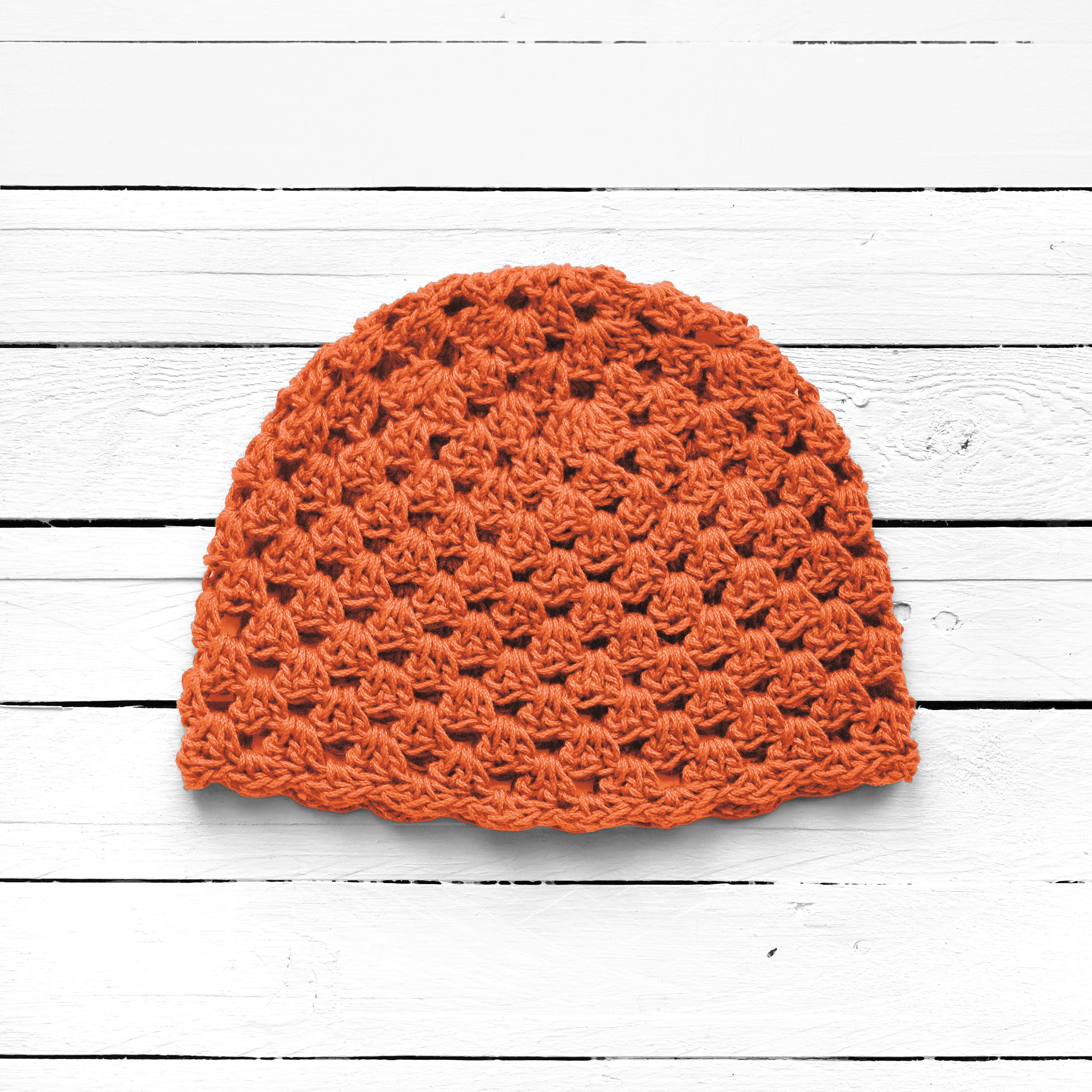 Orange crochet beanie on a white wooden surface.