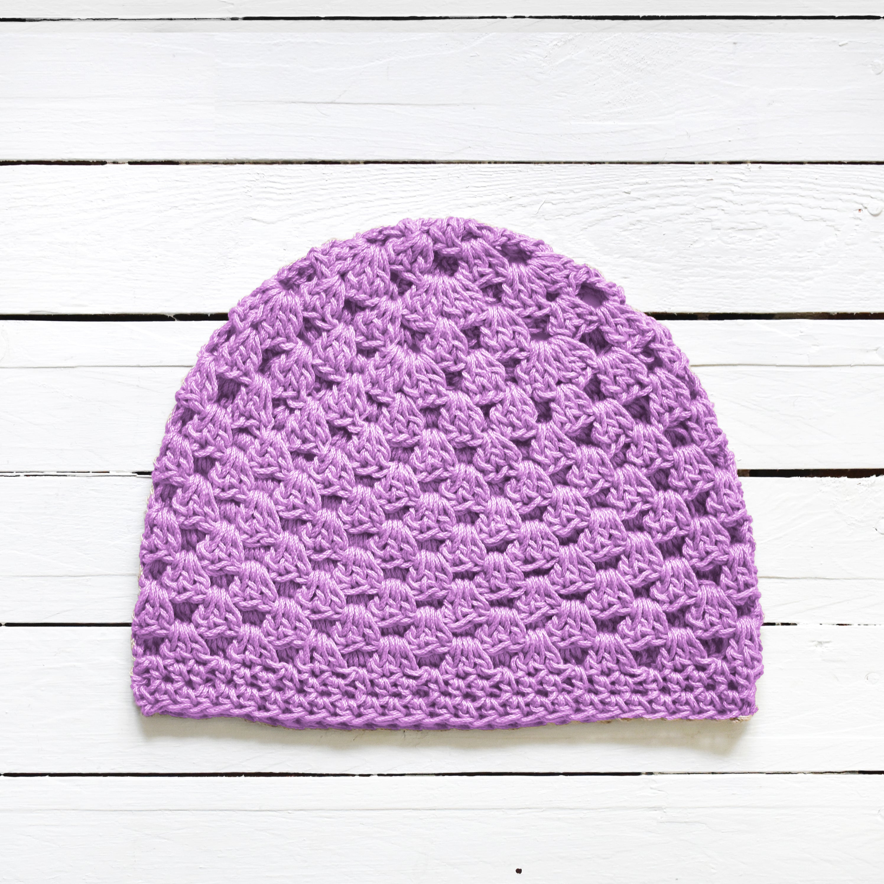 Light purple crocheted beanie on a white wooden surface.