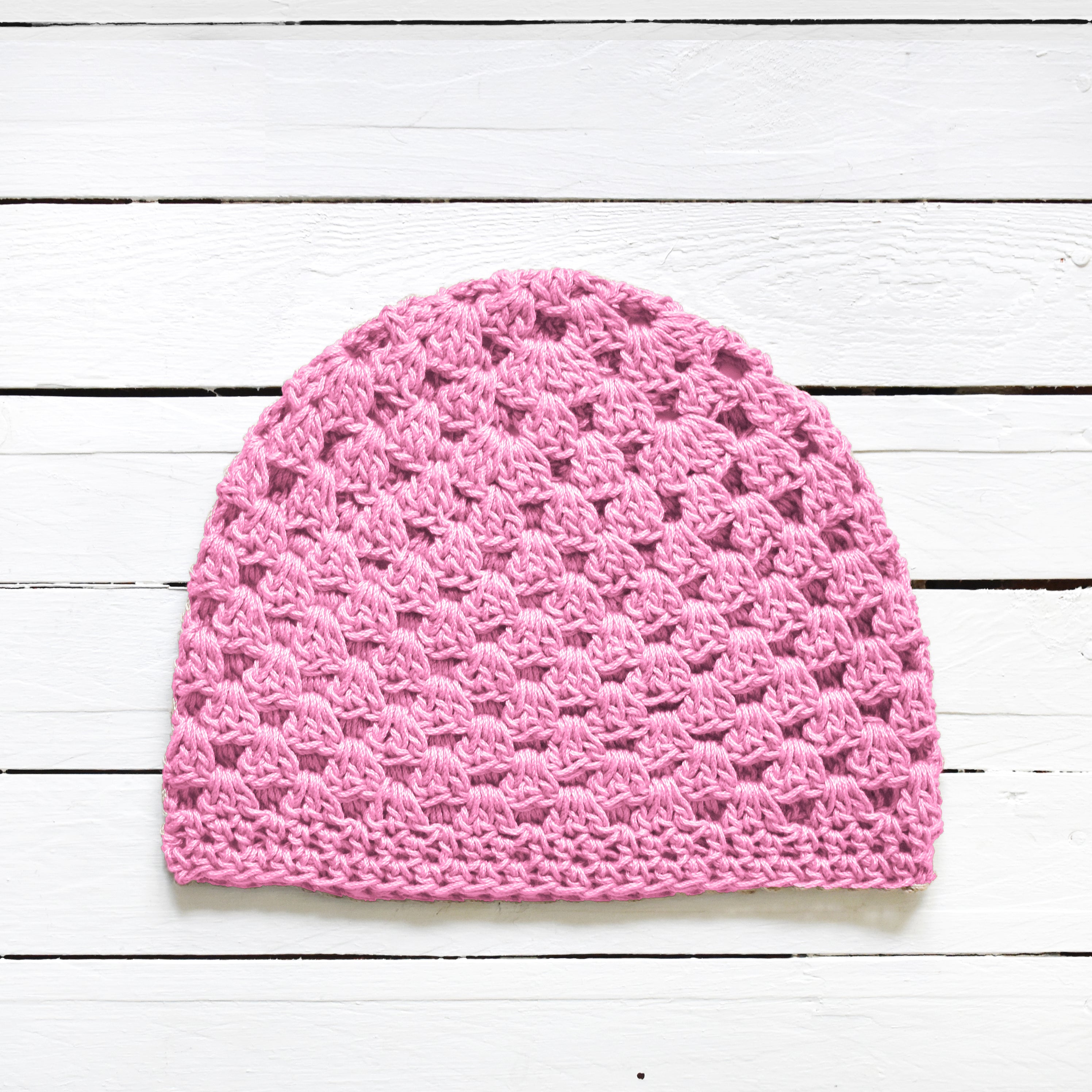 Pink crocheted beanie on a white wooden surface.