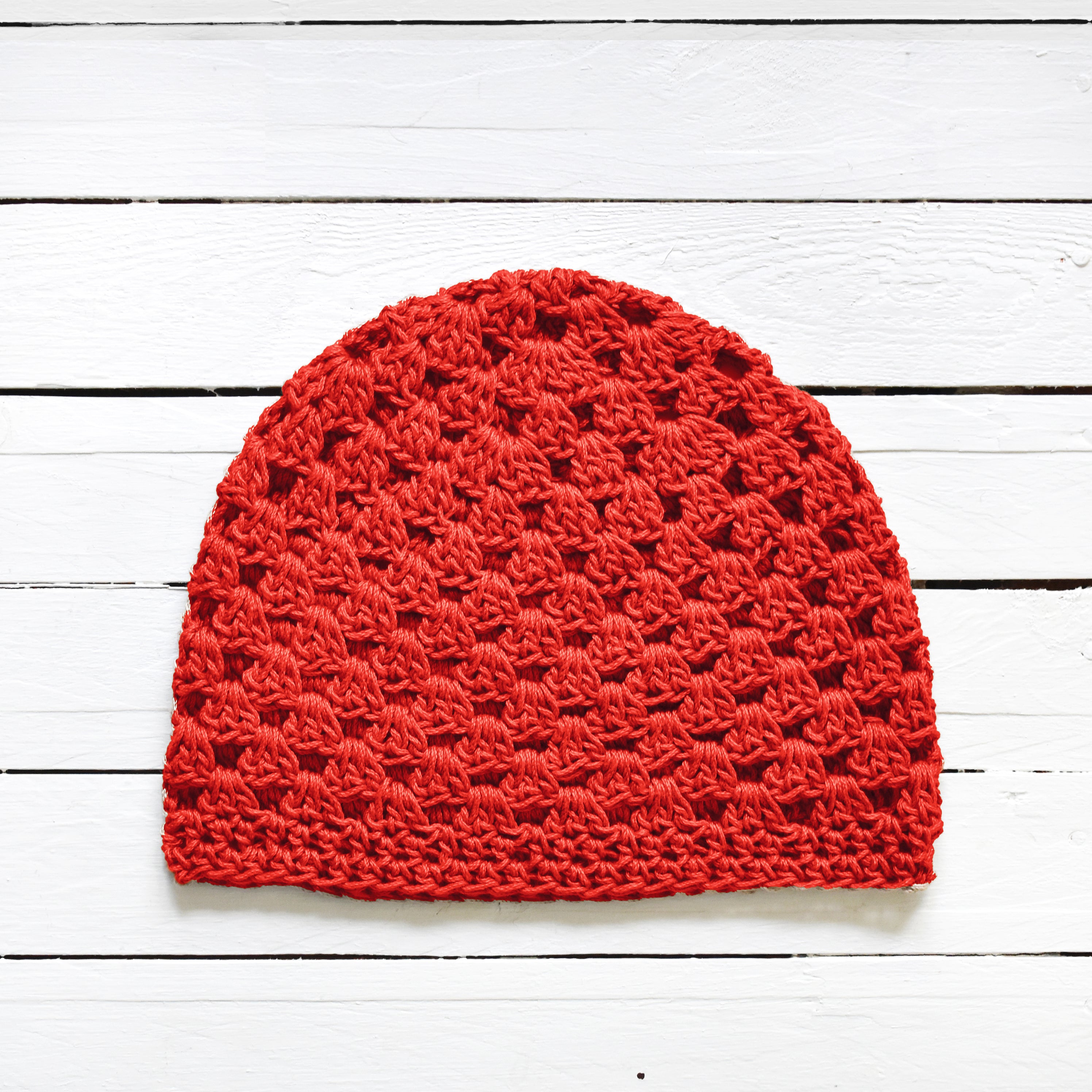Bright red crochet beanie on a white wooden surface.