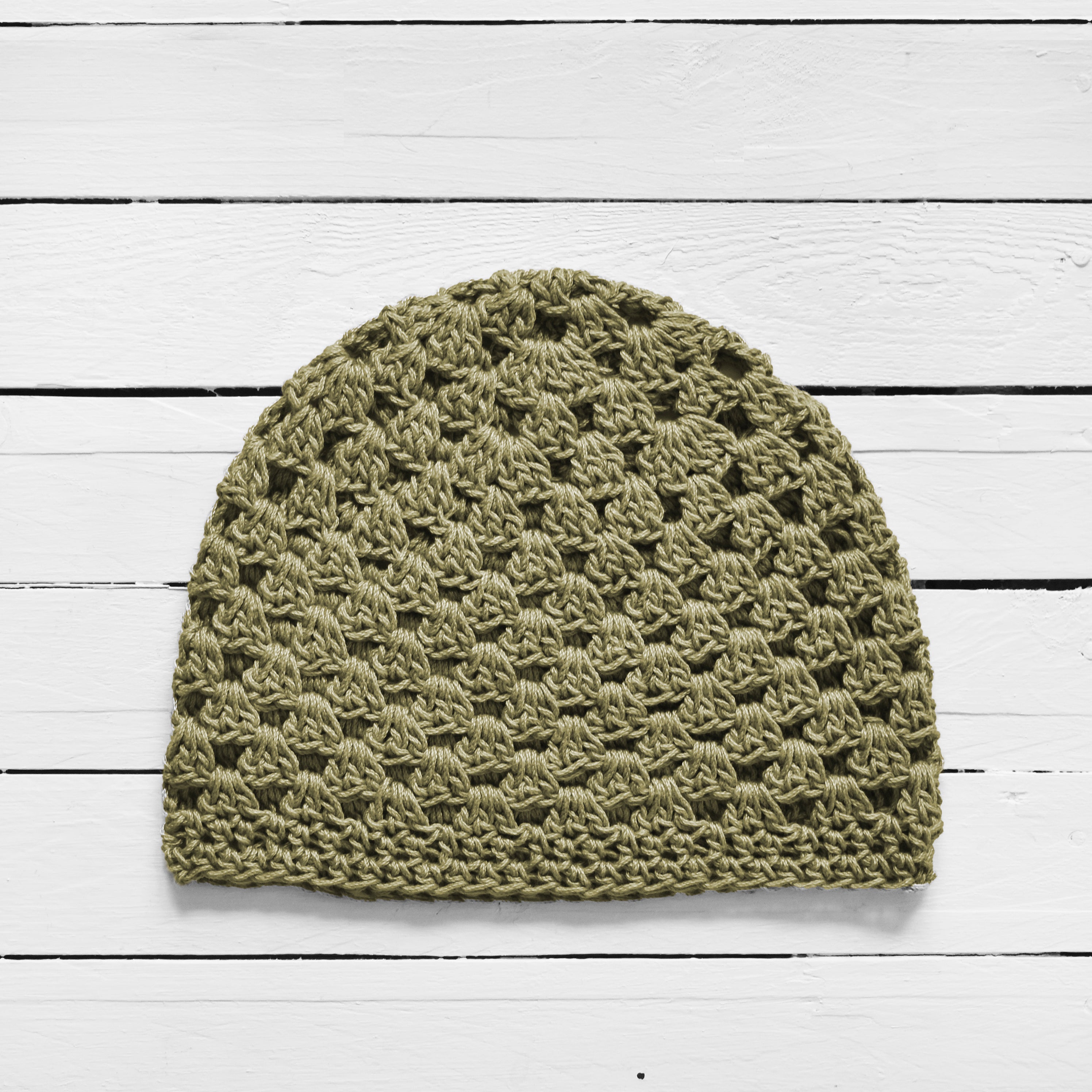 Sage green crochet beanie on a white wooden surface.