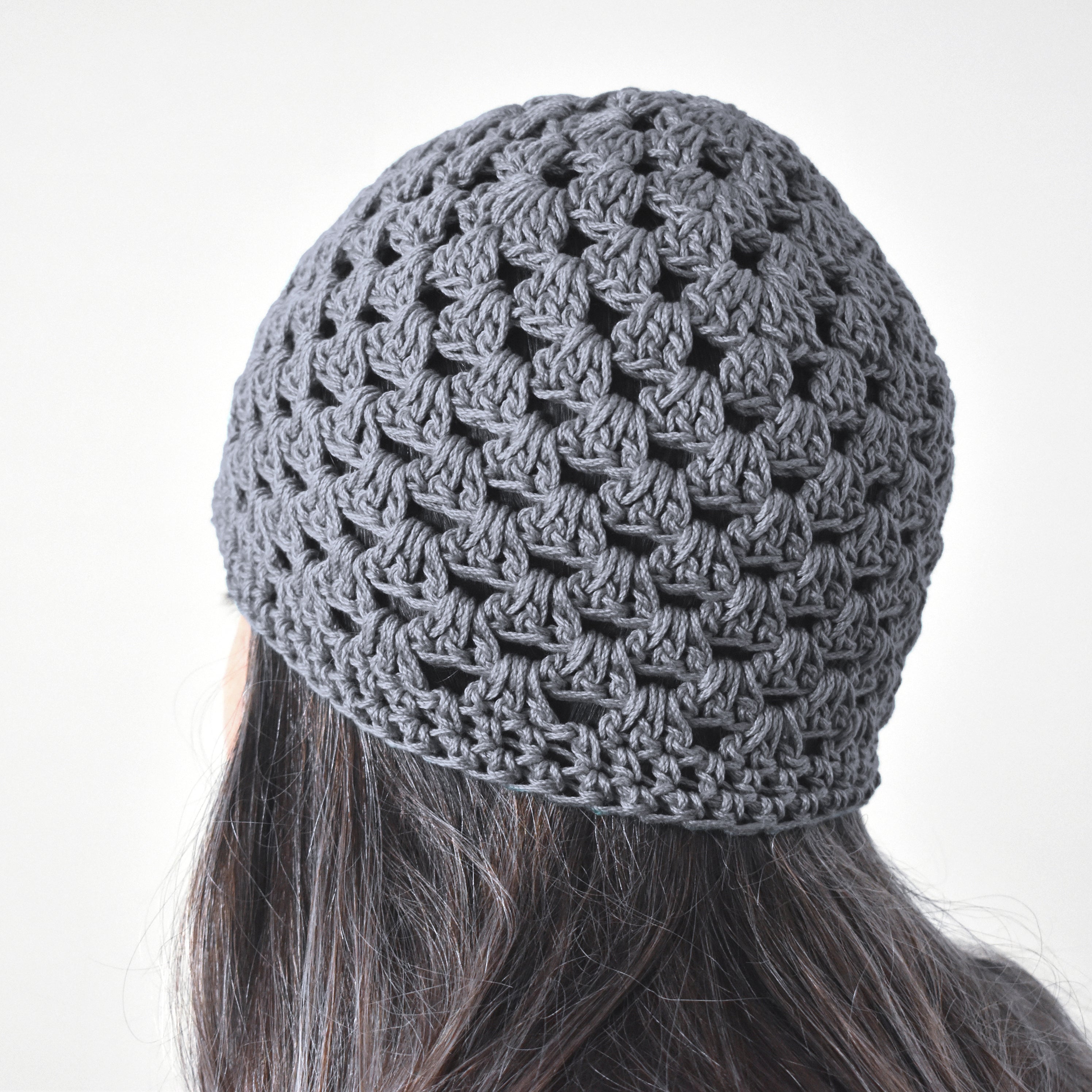 Gray knitted beanie worn by a person with long hair on a white background.
