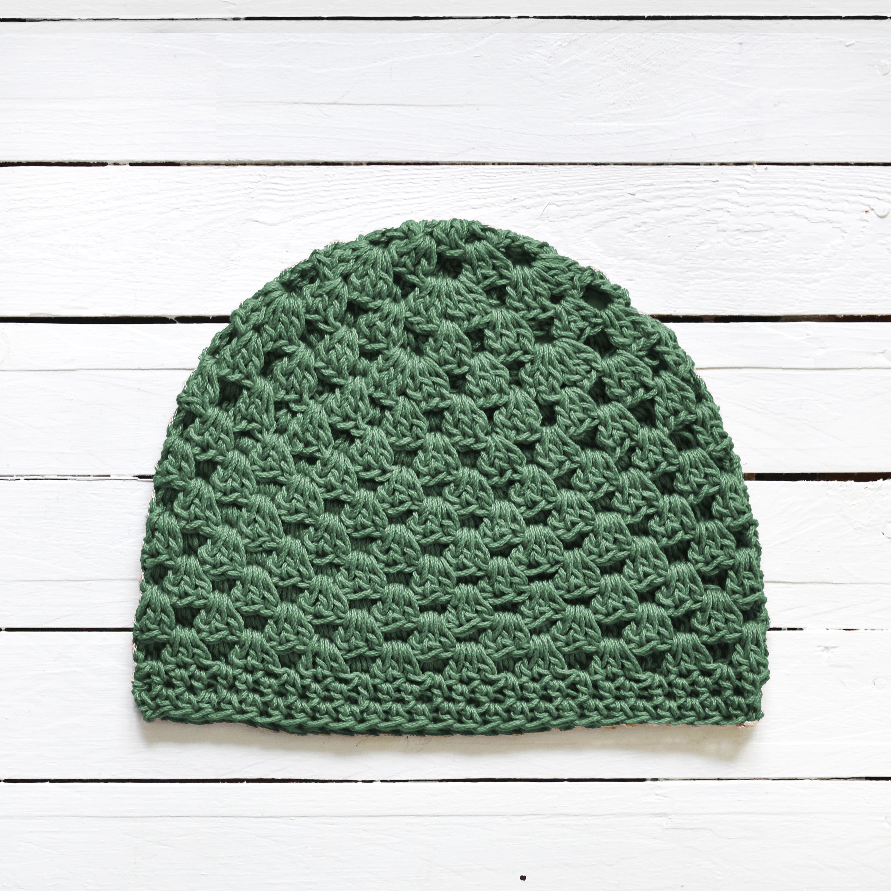 Green crochet beanie on a white wooden surface.