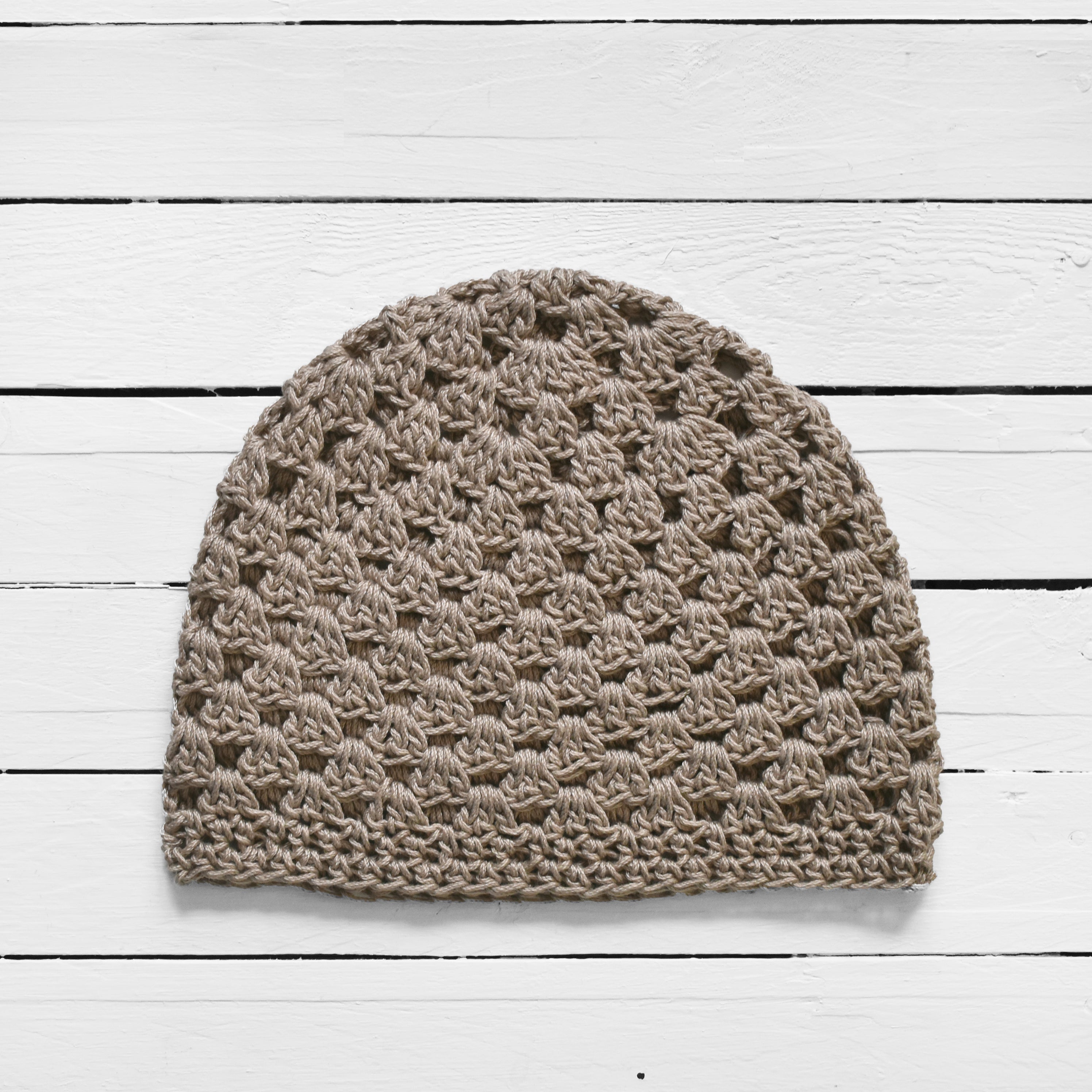 Taupe crochet beanie on a white wooden surface.
