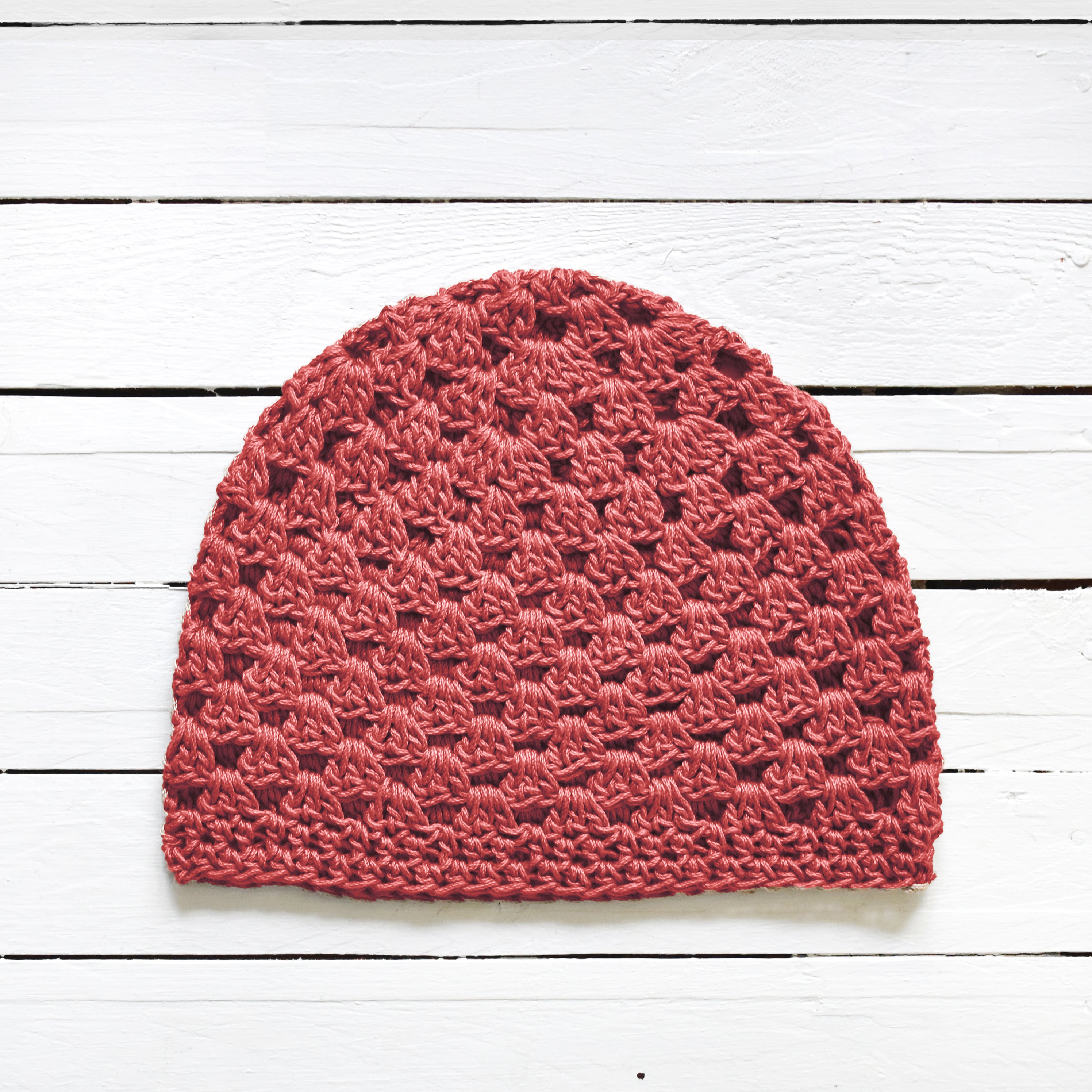 Terracotta pink crochet beanie on a white wooden surface.