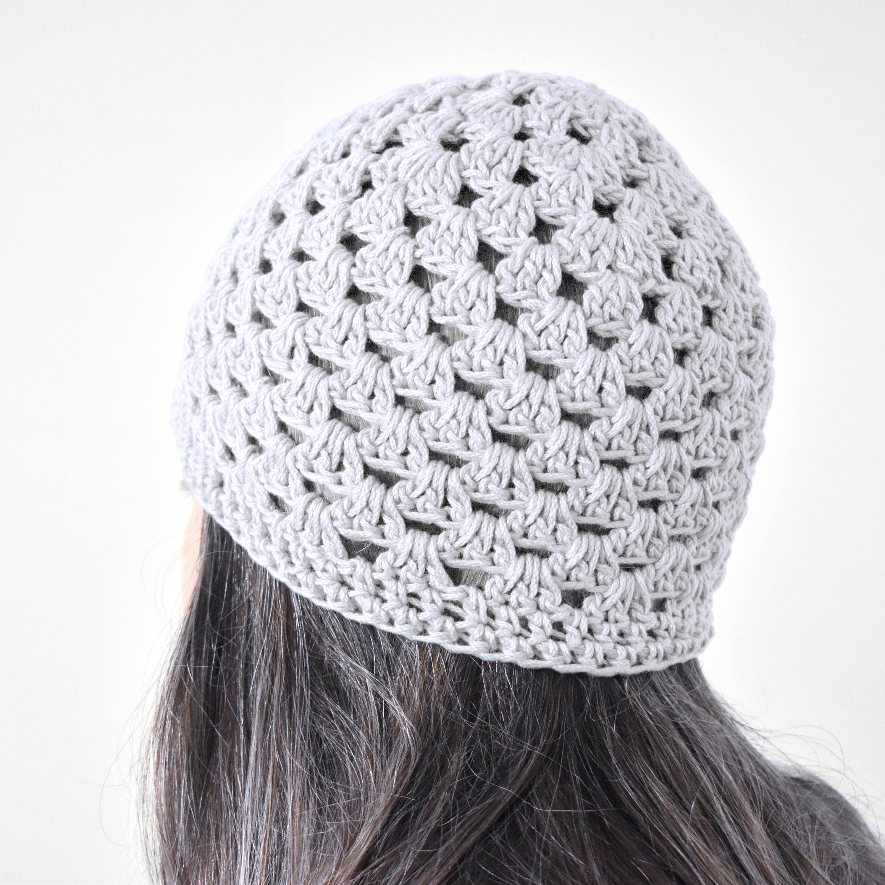 White knitted beanie worn by a person with dark hair on a white background.