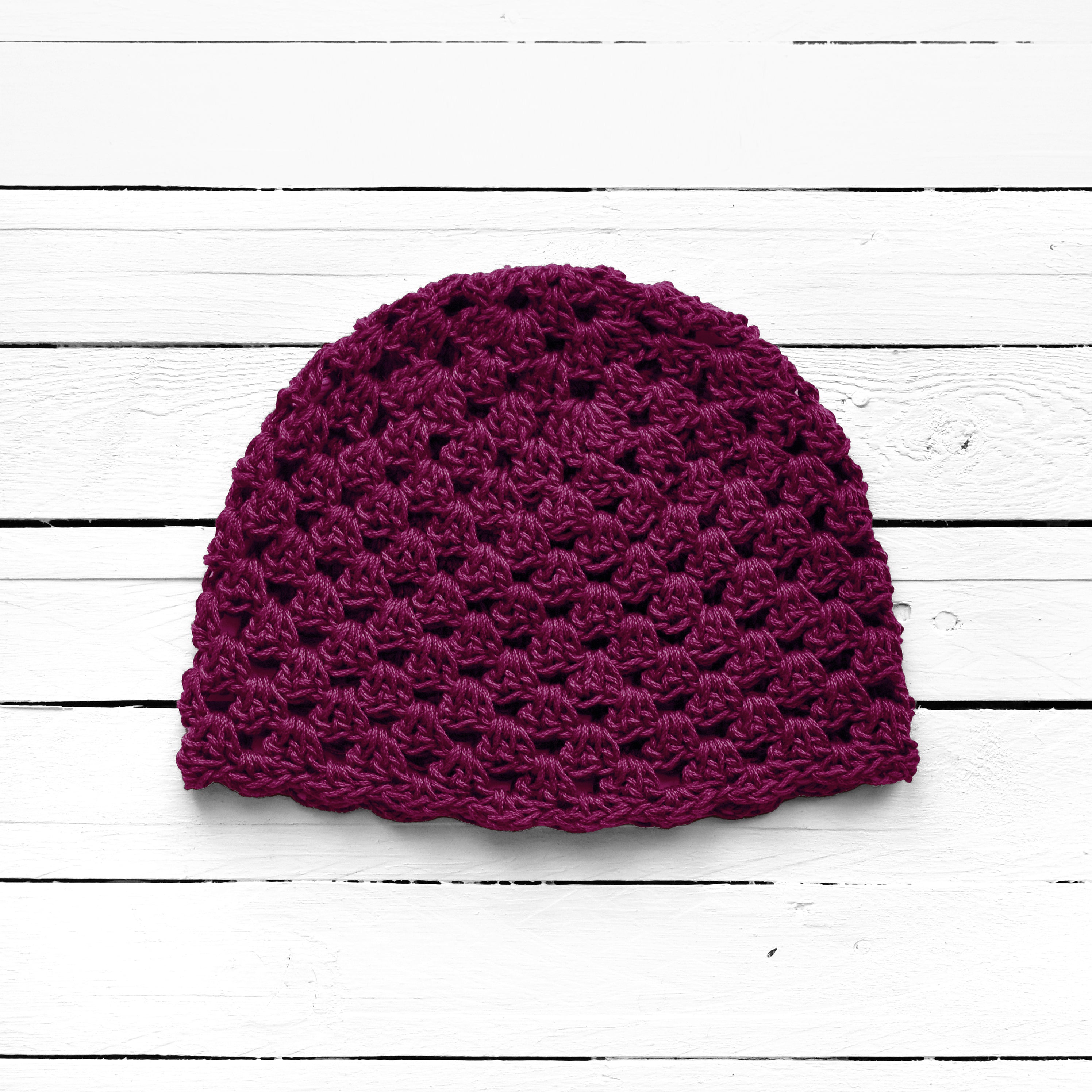 Dark purple crochet beanie on a white wooden surface.