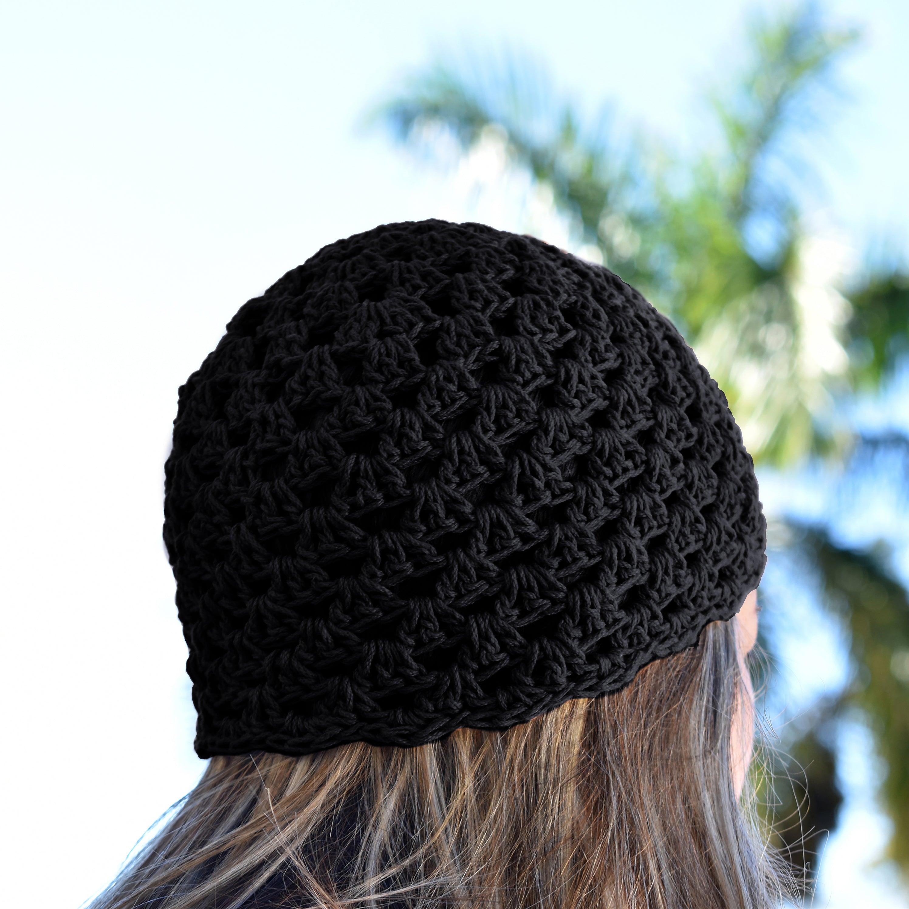 Black knitted beanie worn by a person with blurred greenery in the background.