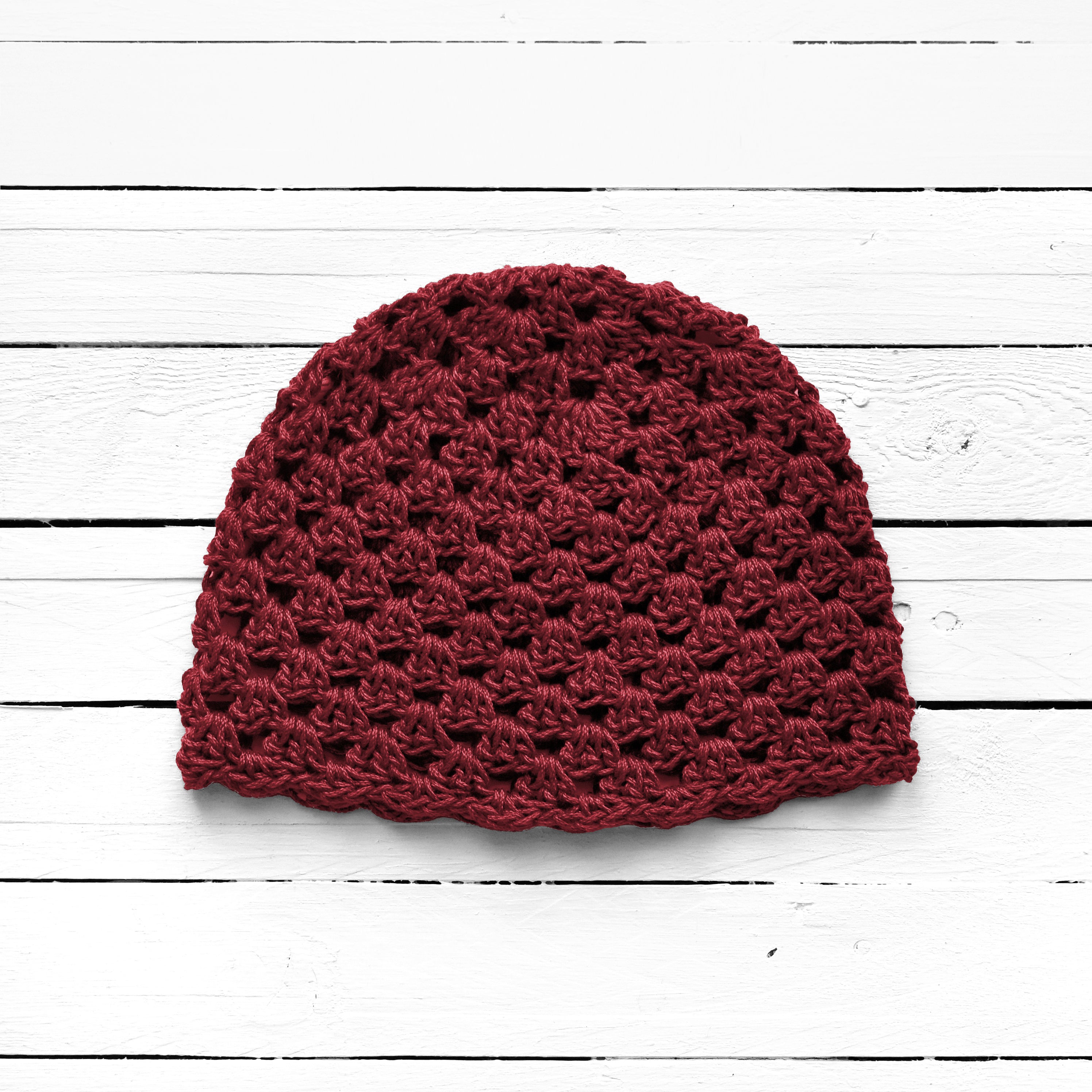 Maroon crochet beanie on a white wooden surface.