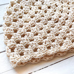 Close-up of a beige crocheted hat on a wooden surface.