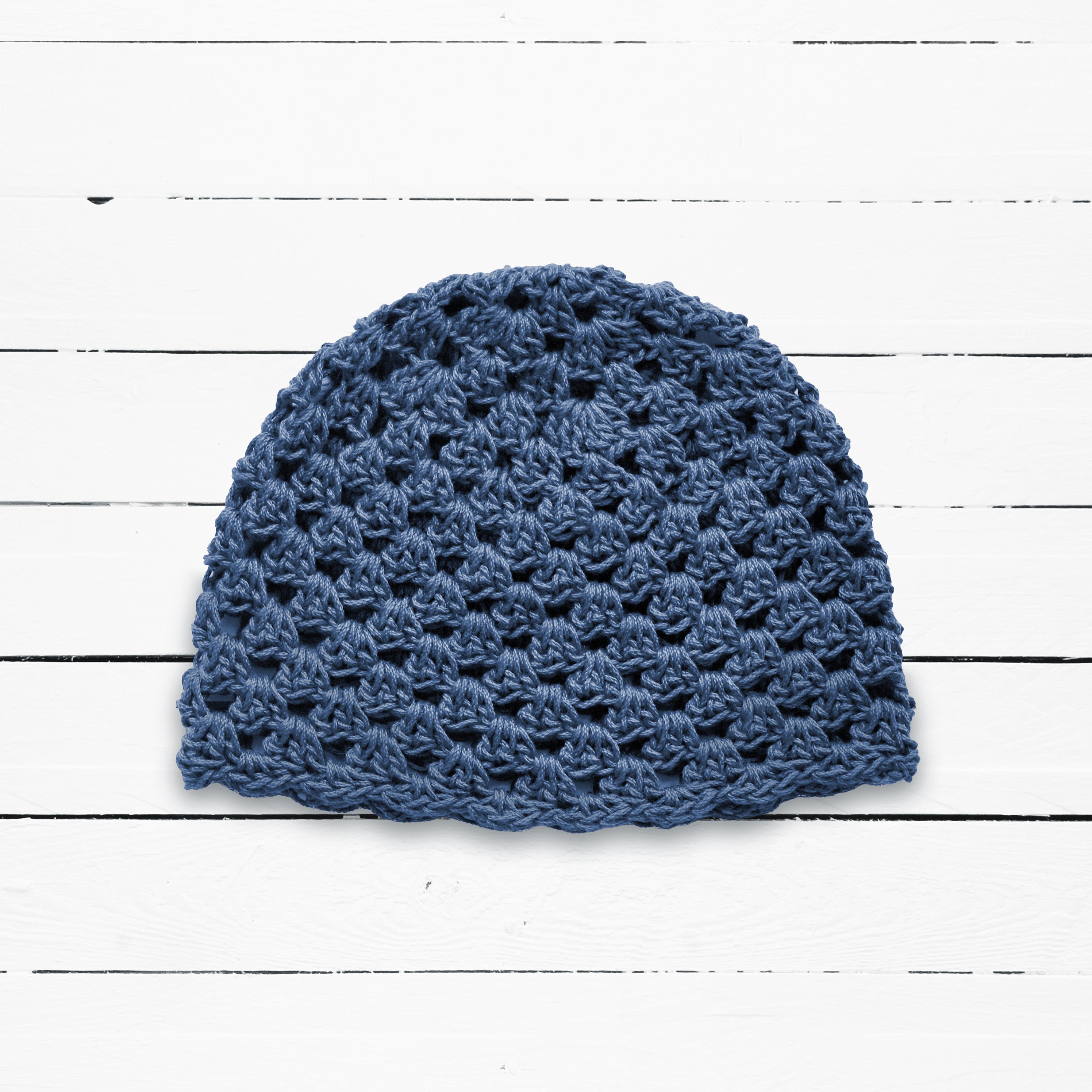 Gray-blue crocheted beanie on a white wooden surface.