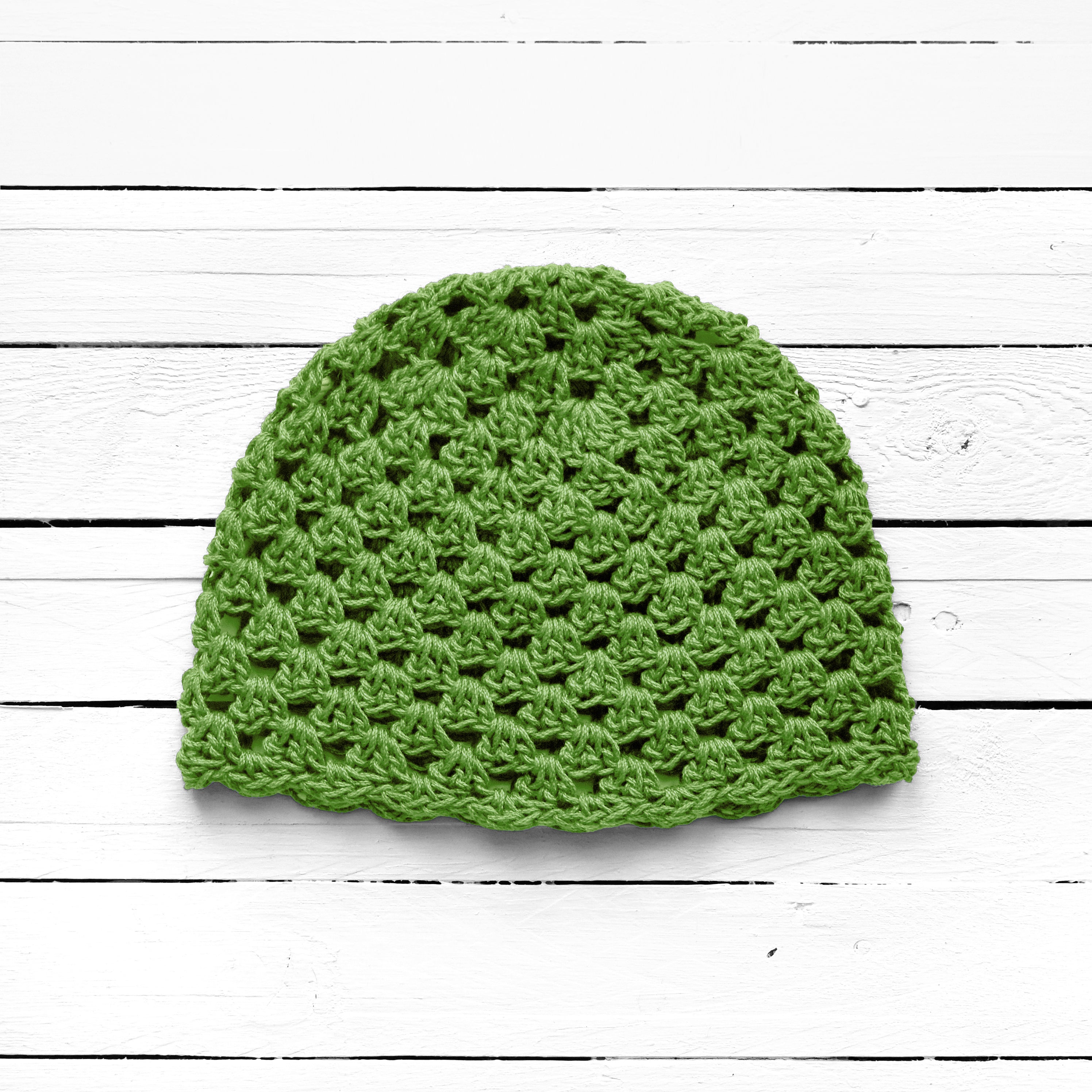 Green crochet hat on a white wooden surface.