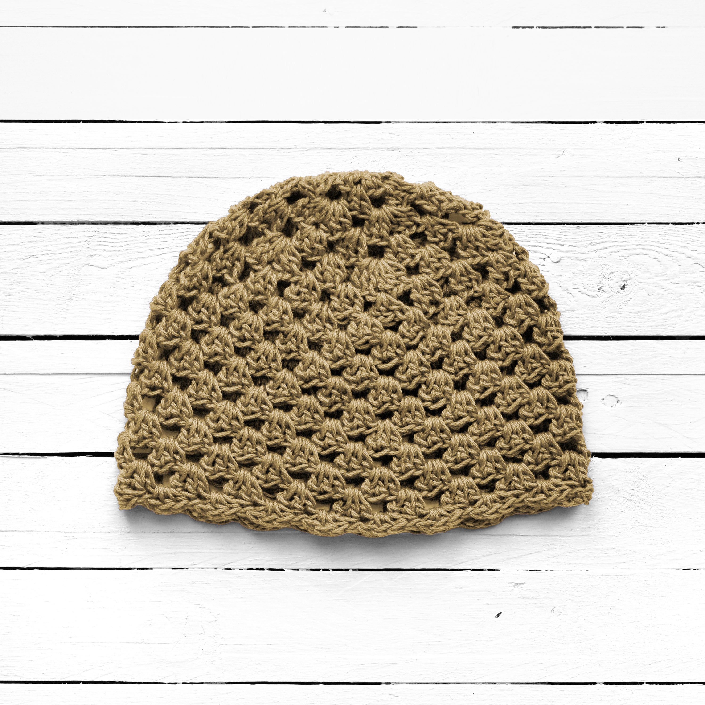 Tan crochet beanie on a white wooden surface.