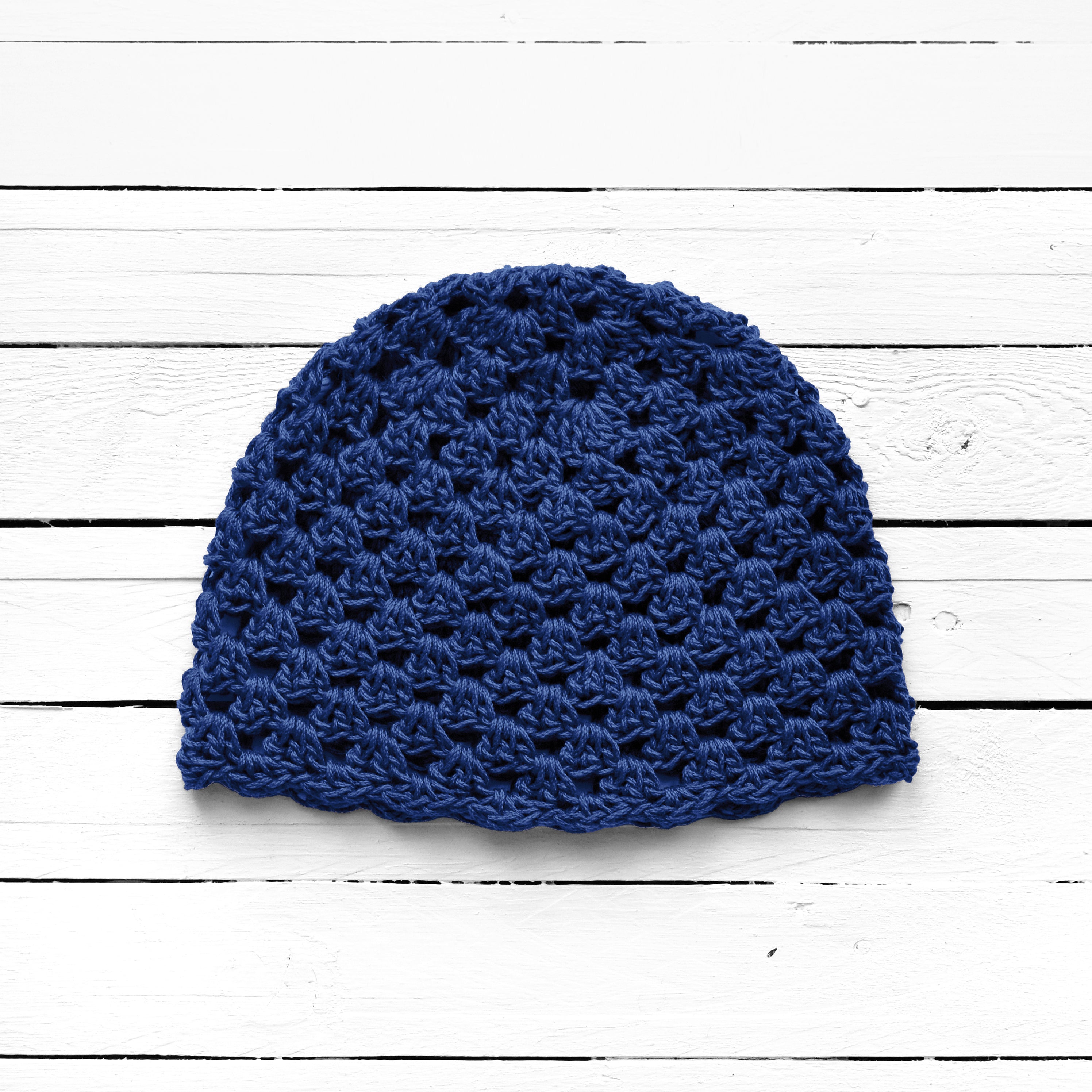 Blue crocheted beanie on a white wooden surface.
