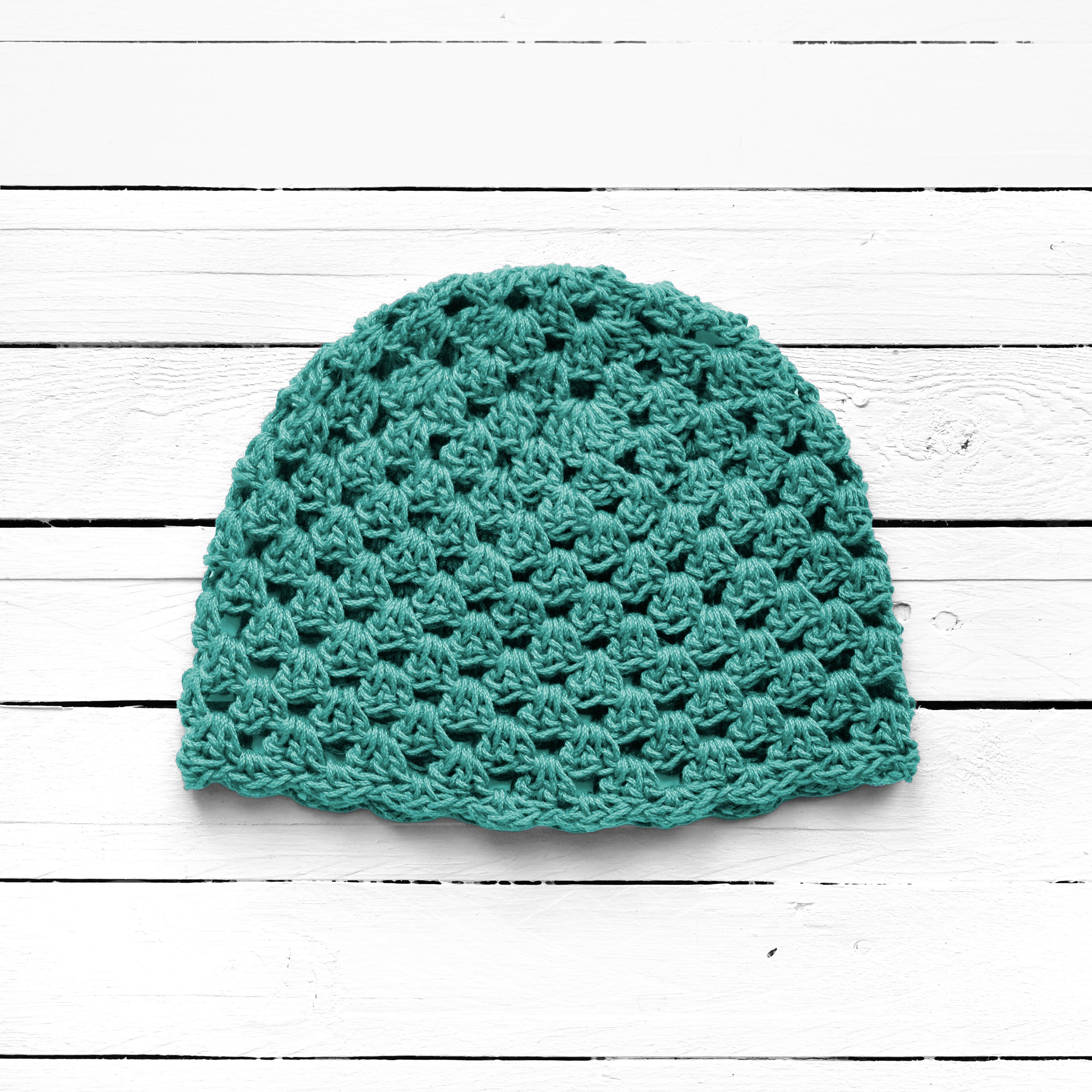 Teal crochet beanie on a white wooden surface.