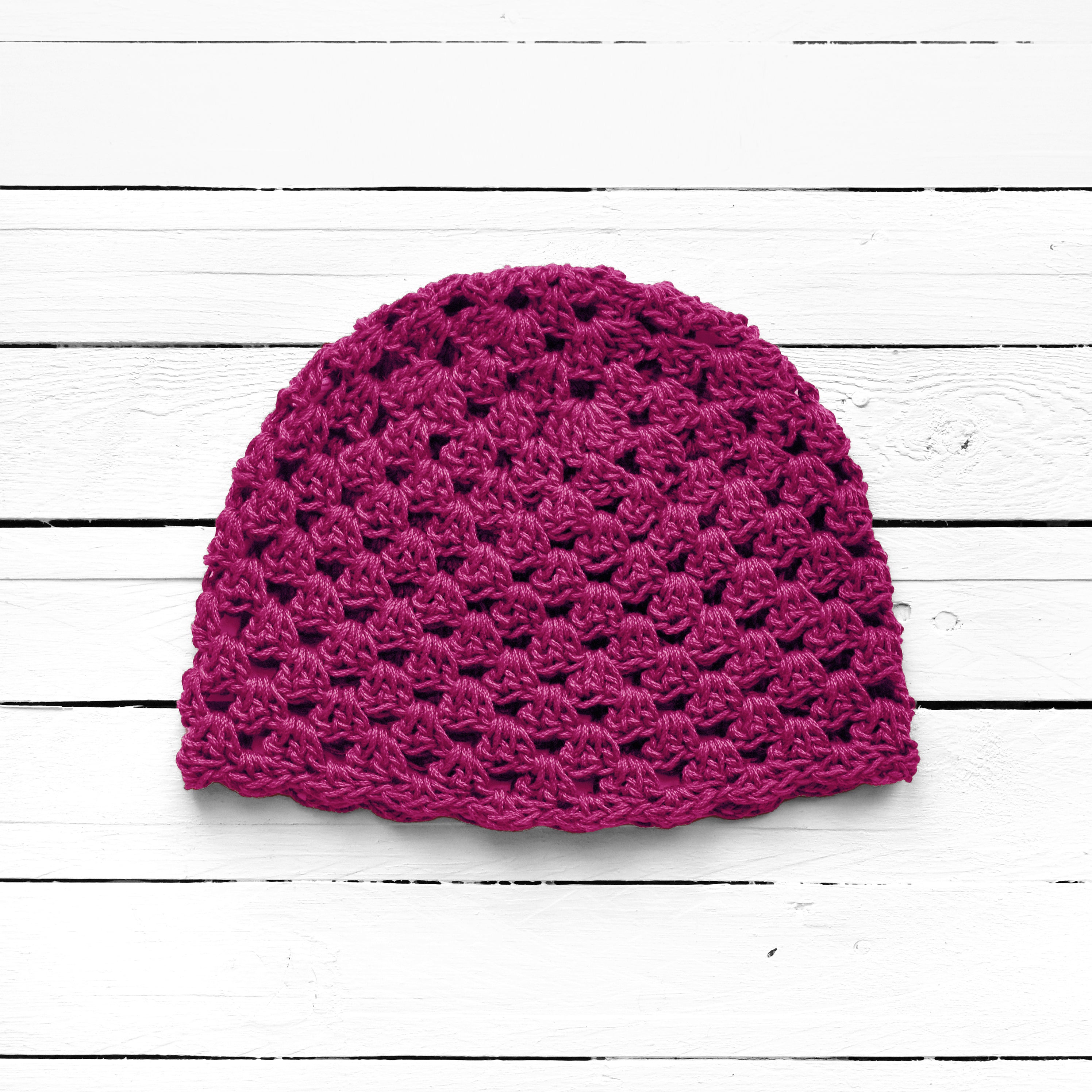Magenta pink crochet bea.nie on a white wooden surface