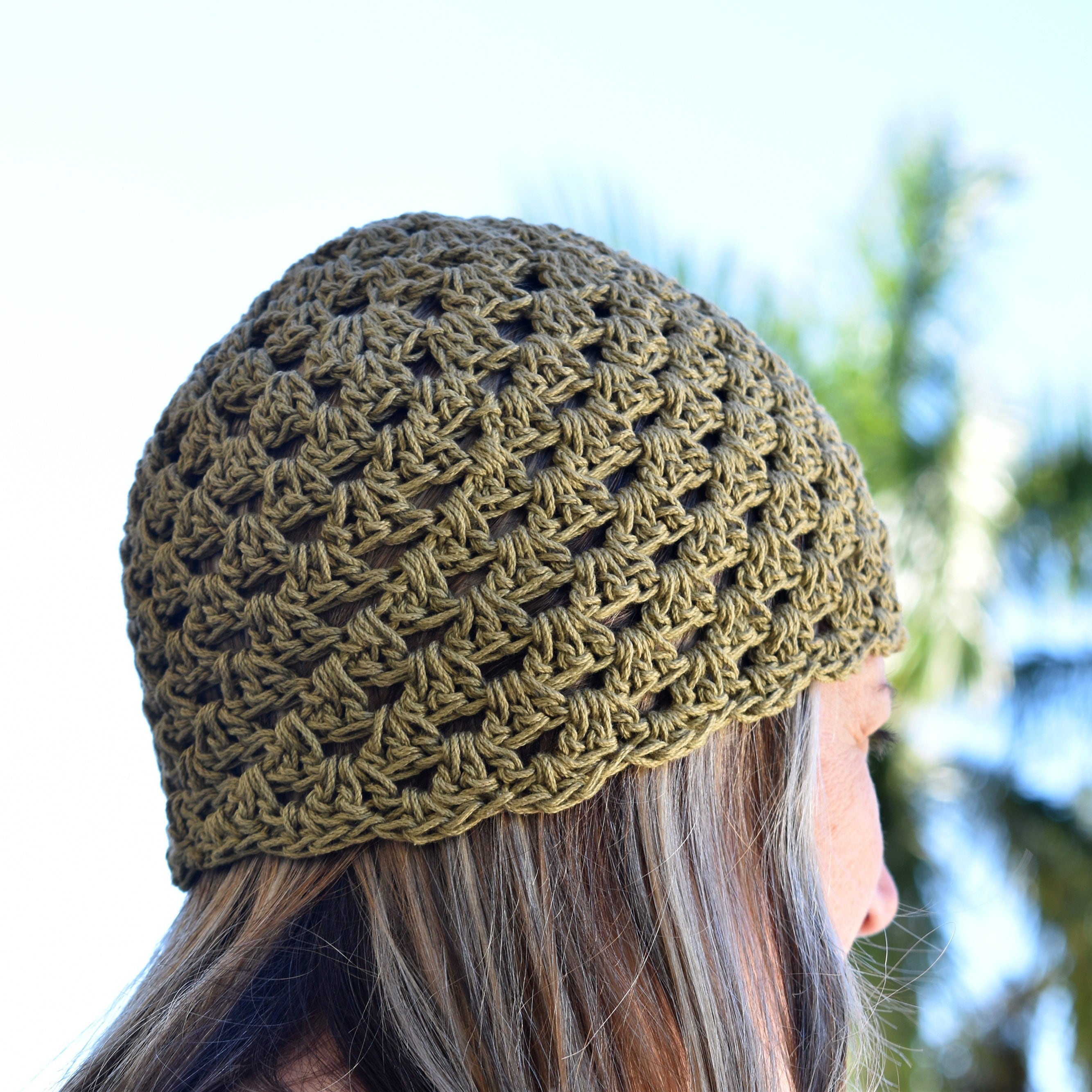 Person wearing a green crochet beanie with blurred natural background.