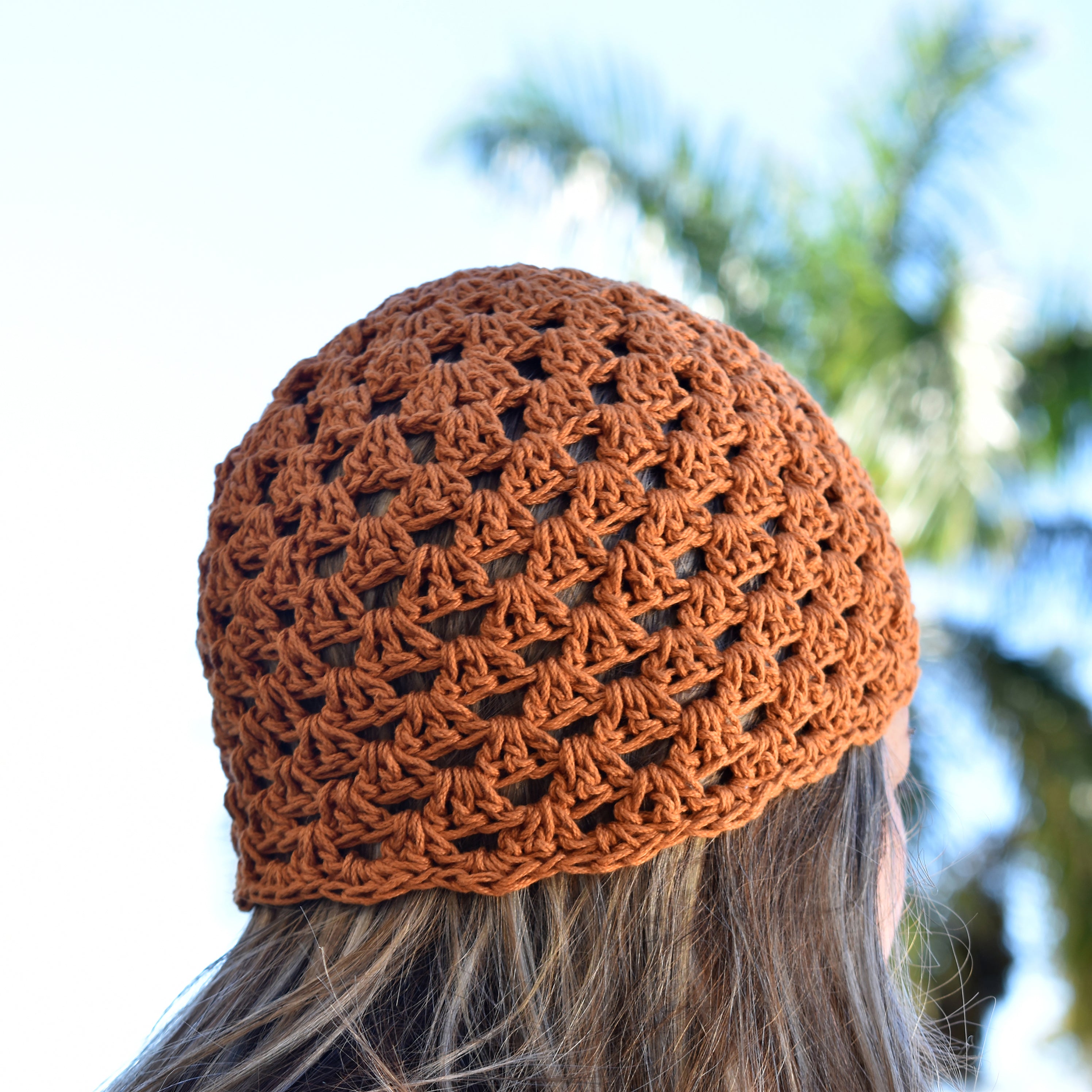 Amber orange crocheted beanie worn by a person with blurred greenery in the background.