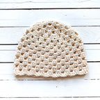 Beige crochet hat on a white wooden surface.