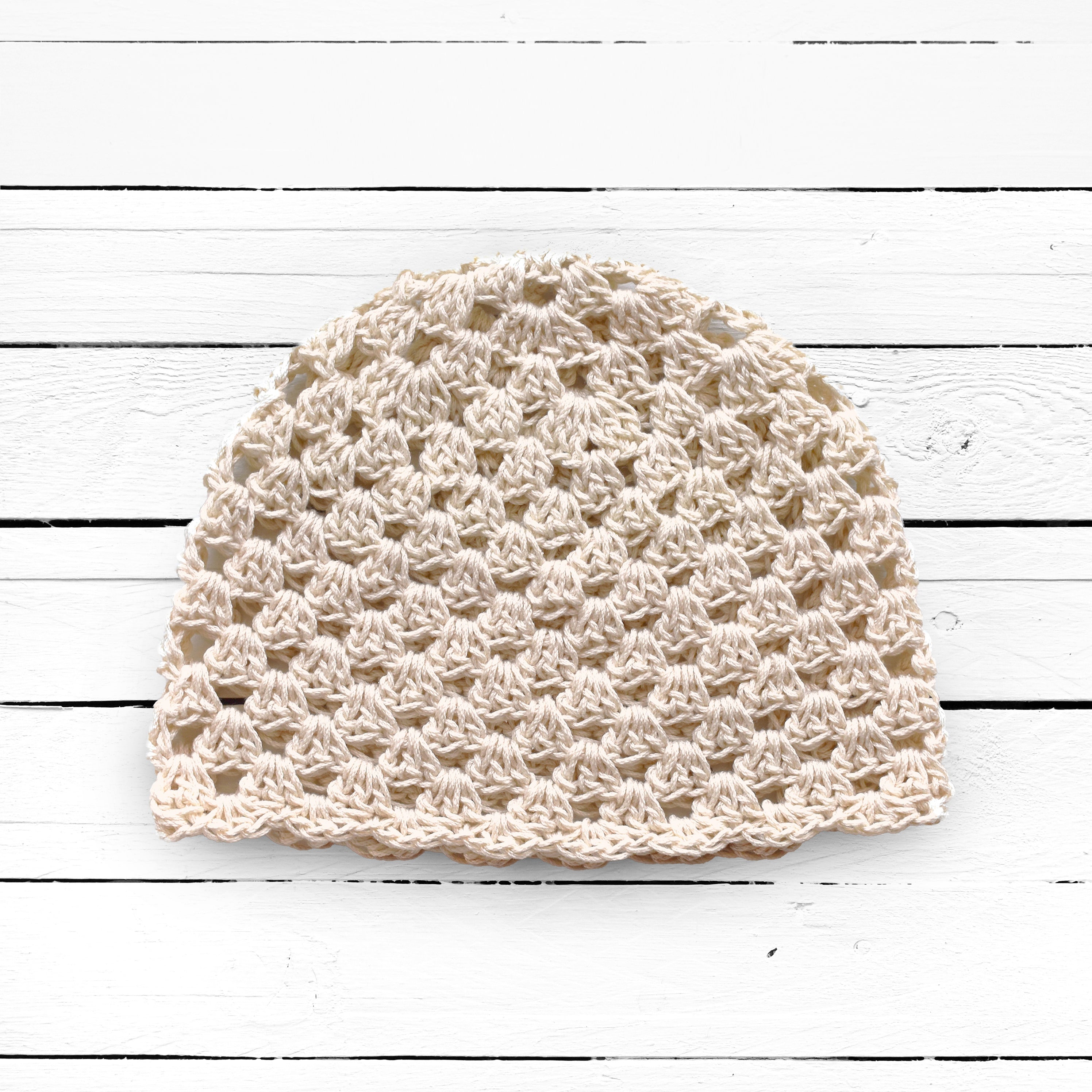 Beige crochet hat on a white wooden surface.
