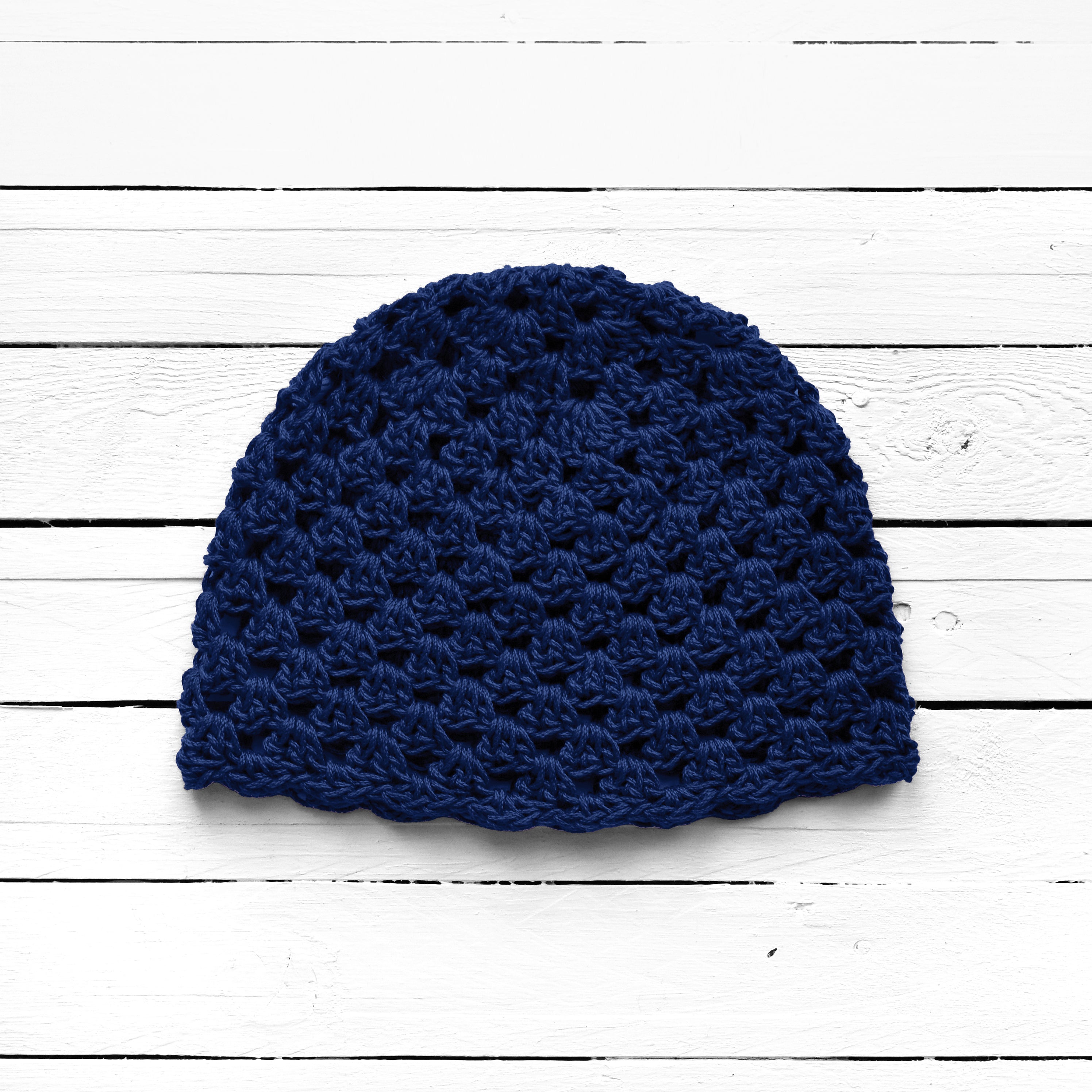 Blue knitted beanie on a white wooden surface.