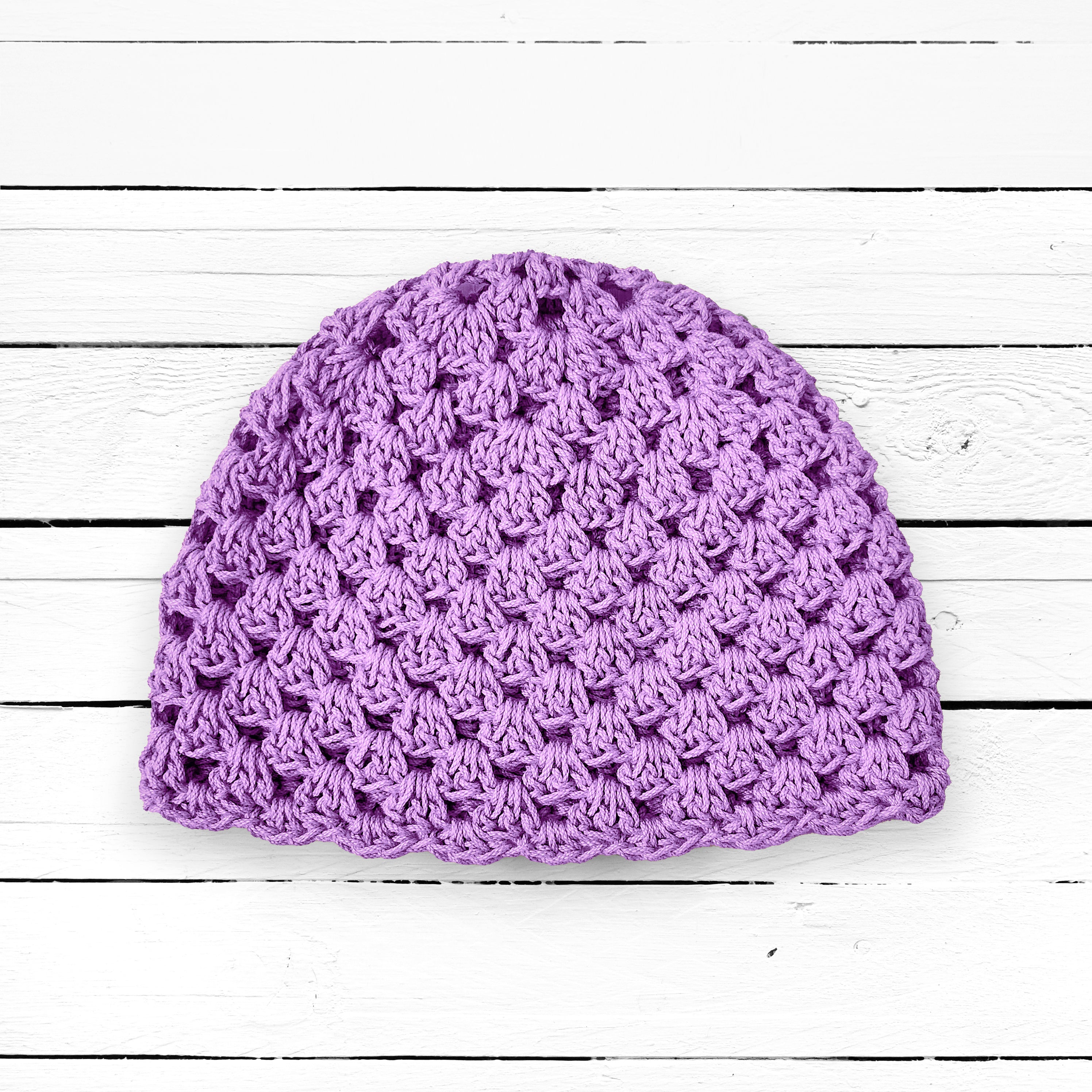 Light purple crocheted beanie on a white wooden surface.