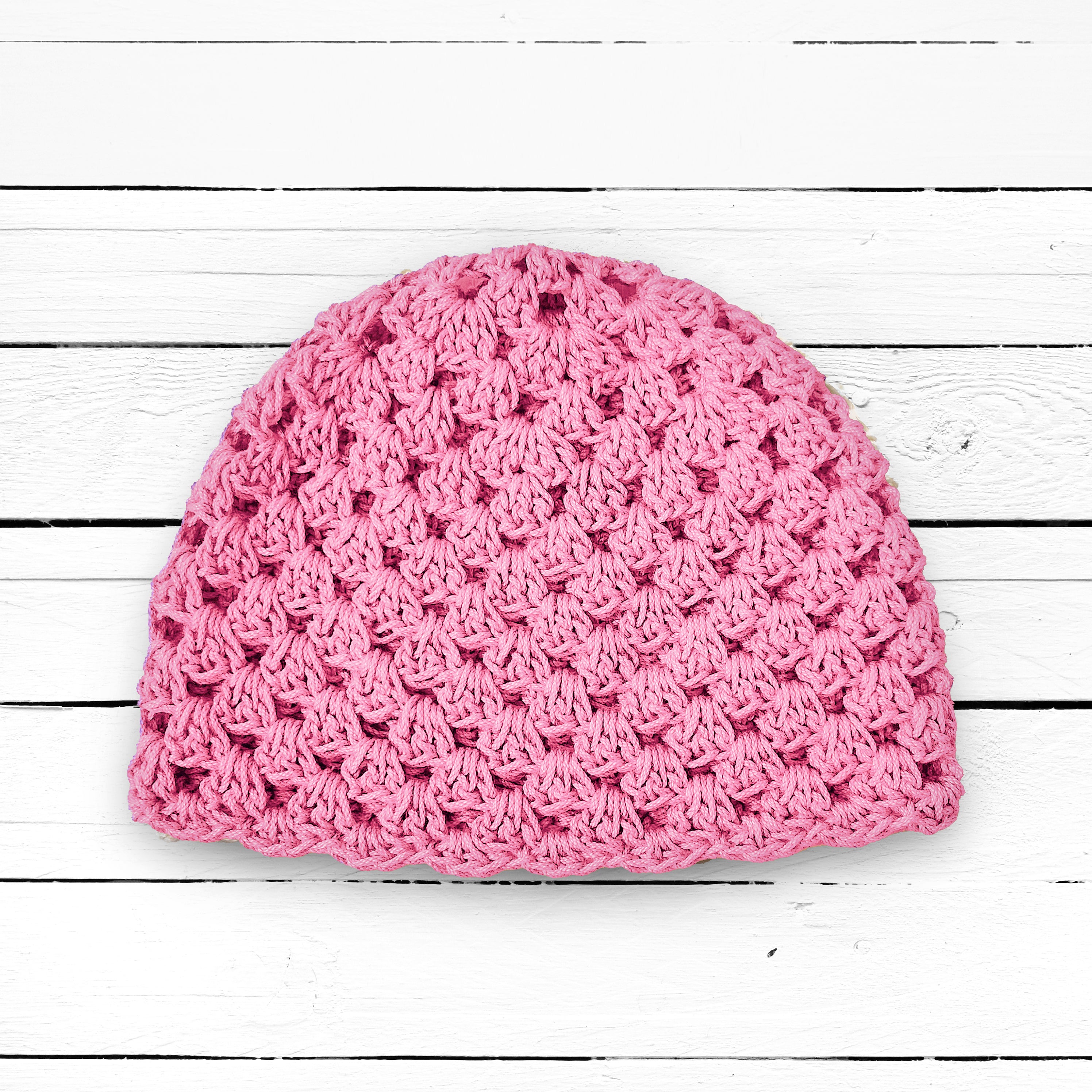 Pink crocheted beanie on a white wooden surface.