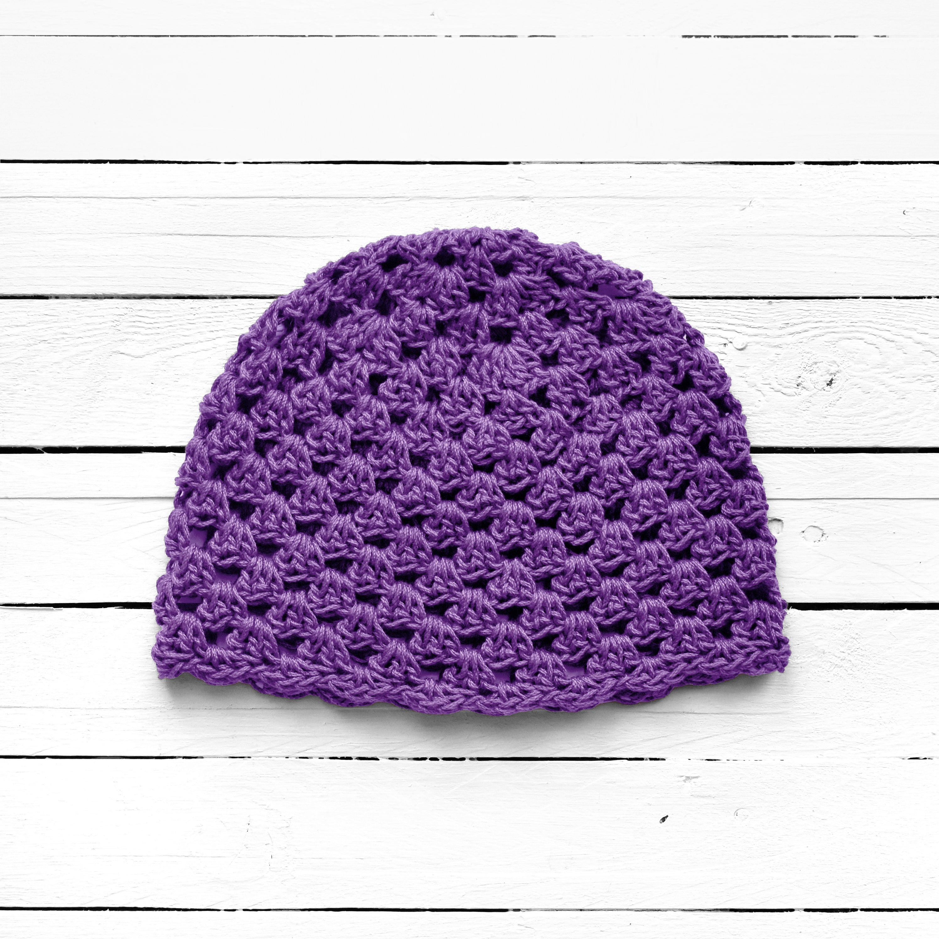 Purple crocheted beanie on a white wooden surface.