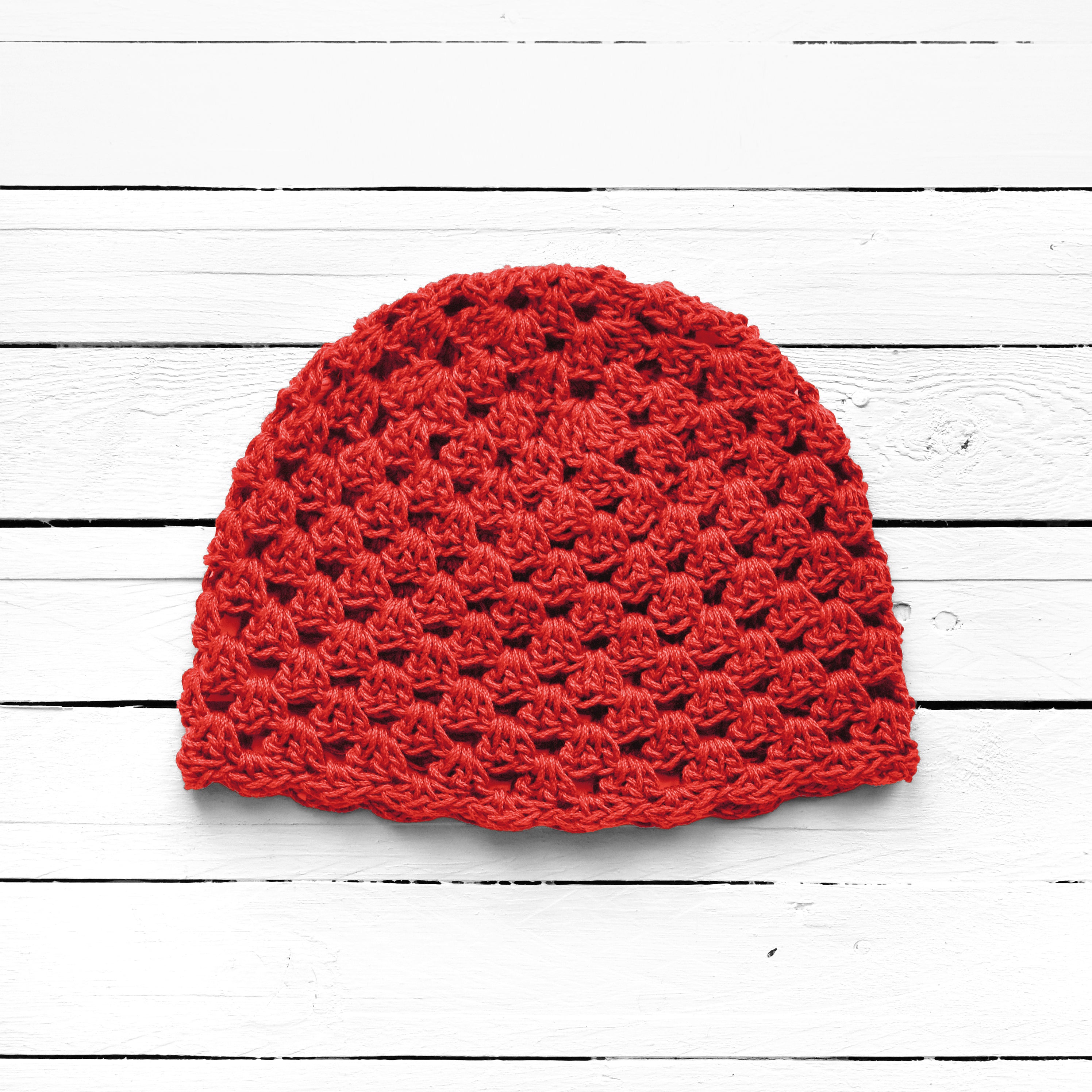 Bright red crochet beanie on a white wooden surface.